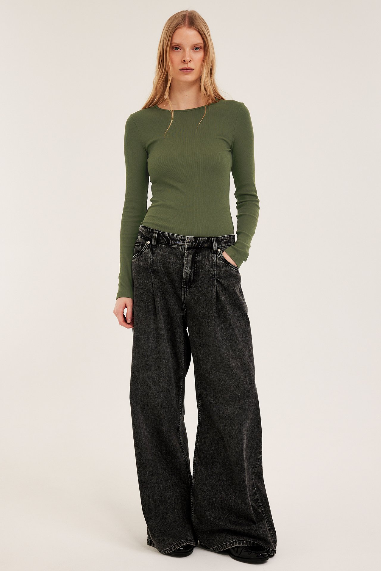 Framifrån: kvinna i khakigrön ribbad långärmad topp och mörkgrå vida jeans.