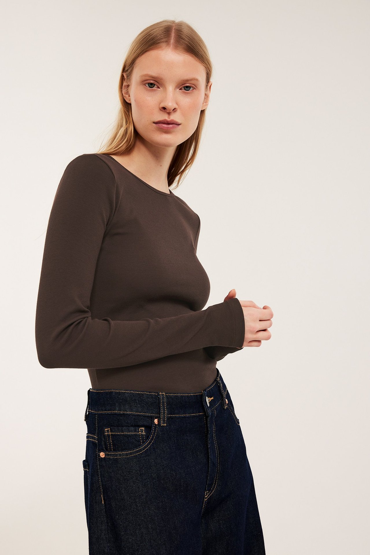 Widok z przodu: kobieta w ciemnobrązowej prążkowanej koszulce z długim rękawem i ciemnoniebieskich dżinsach.