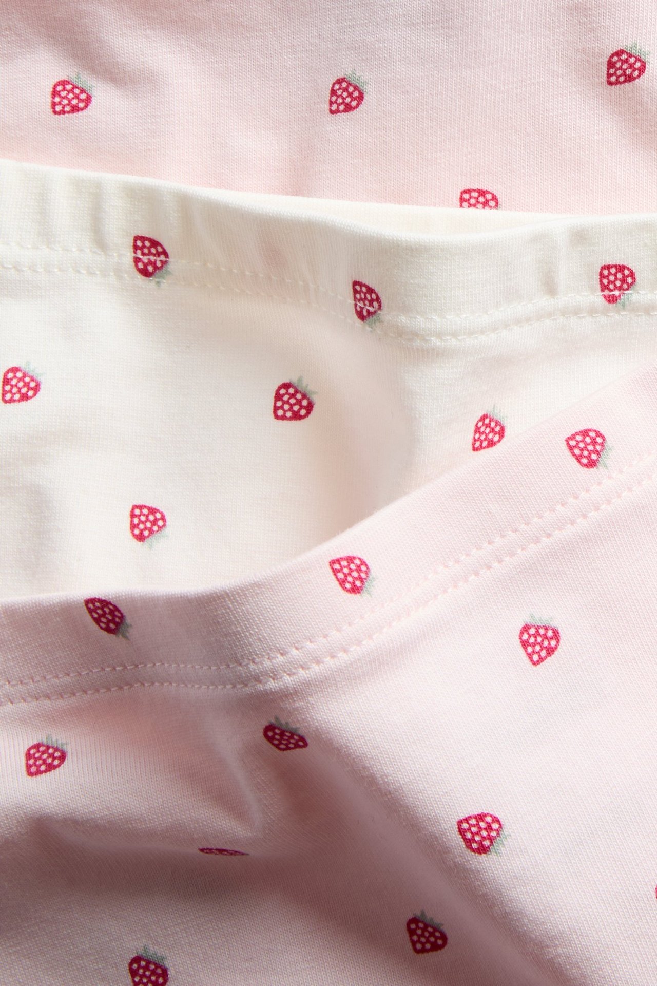 Lähikuva kolmesta parista vaaleanpunaisia ja luonnonvalkoisia lasten bokserialushousuja, joissa on mansikkakuvio.