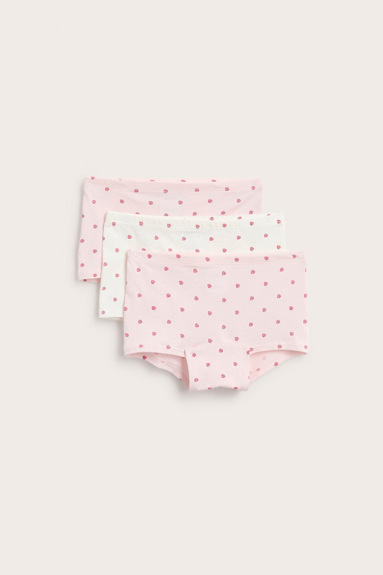 Edestä kolme lapsen vaaleanpunaista ja valkoista mansikkakuvioista bokserihousua.