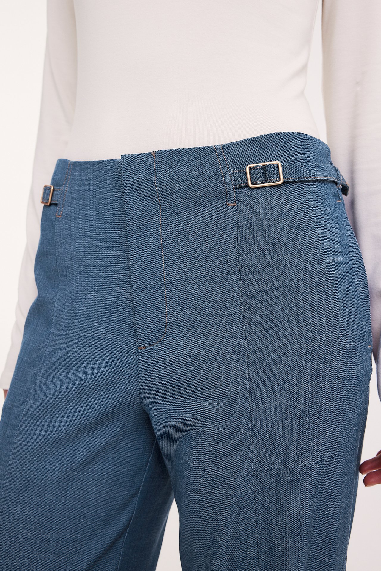 Lähikuva: Nainen vaaleansinisissä leveälahkeisissa housuissa sivusoljilla ja valkoinen pitkähihainen toppi.