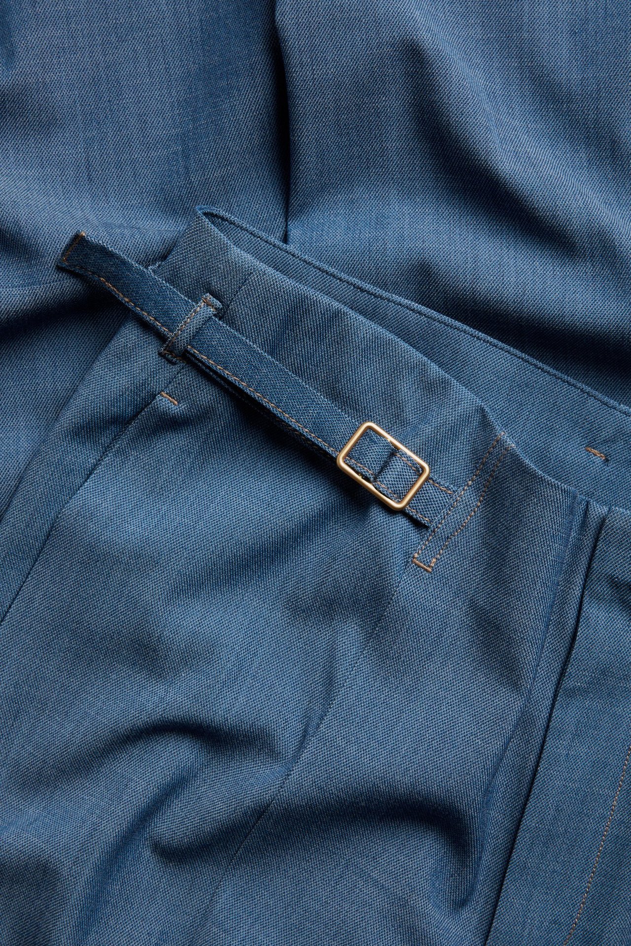 Zbliżenie jasnoniebieskich spodni z szerokimi nogawkami, pokazujące regulowany pasek ze złotą klamrą.