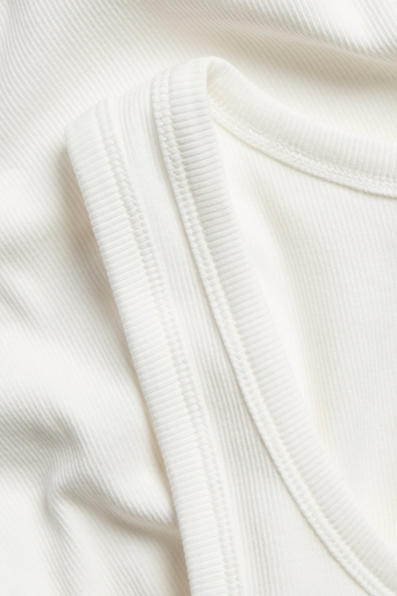 Biały dopasowany basic tank top z cienką ribkową fakturą, zbliżenie z przodu.