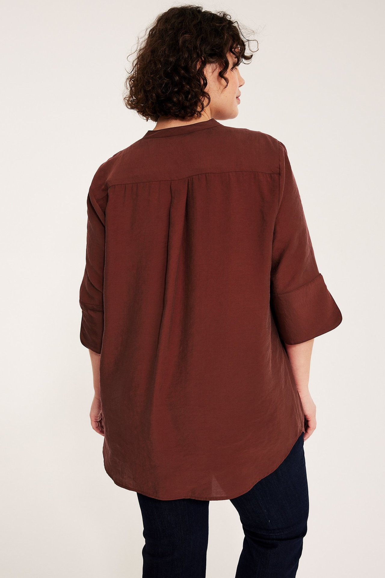 Takakuva: nainen väljässä tummanpunaisessa 3/4-hihaisessa puserossa ja tummissa farkuissa.