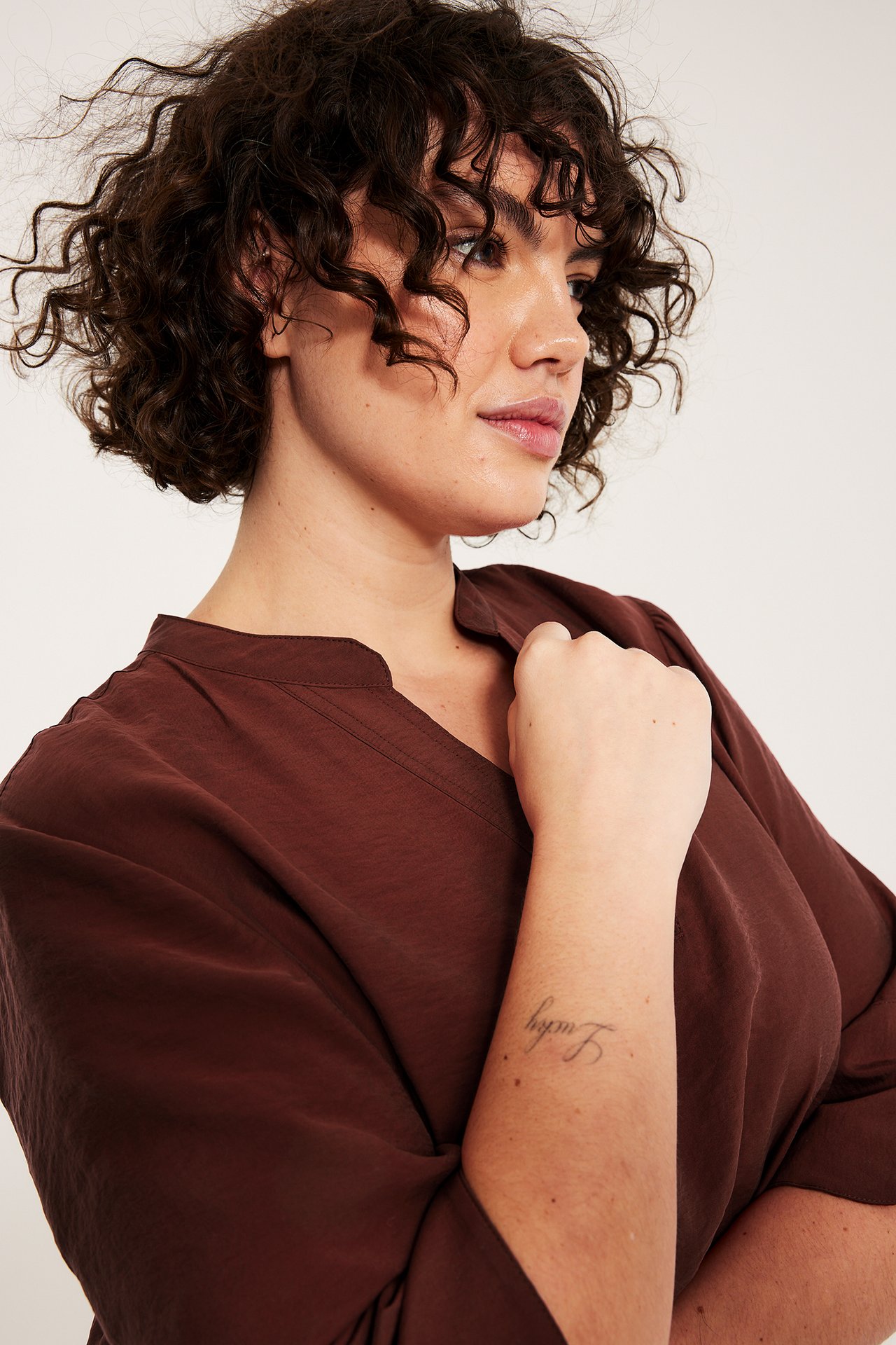 Lähikuva naisesta, jolla on tummanpunainen V-aukkoinen pusero silkkimäisellä laadulla.