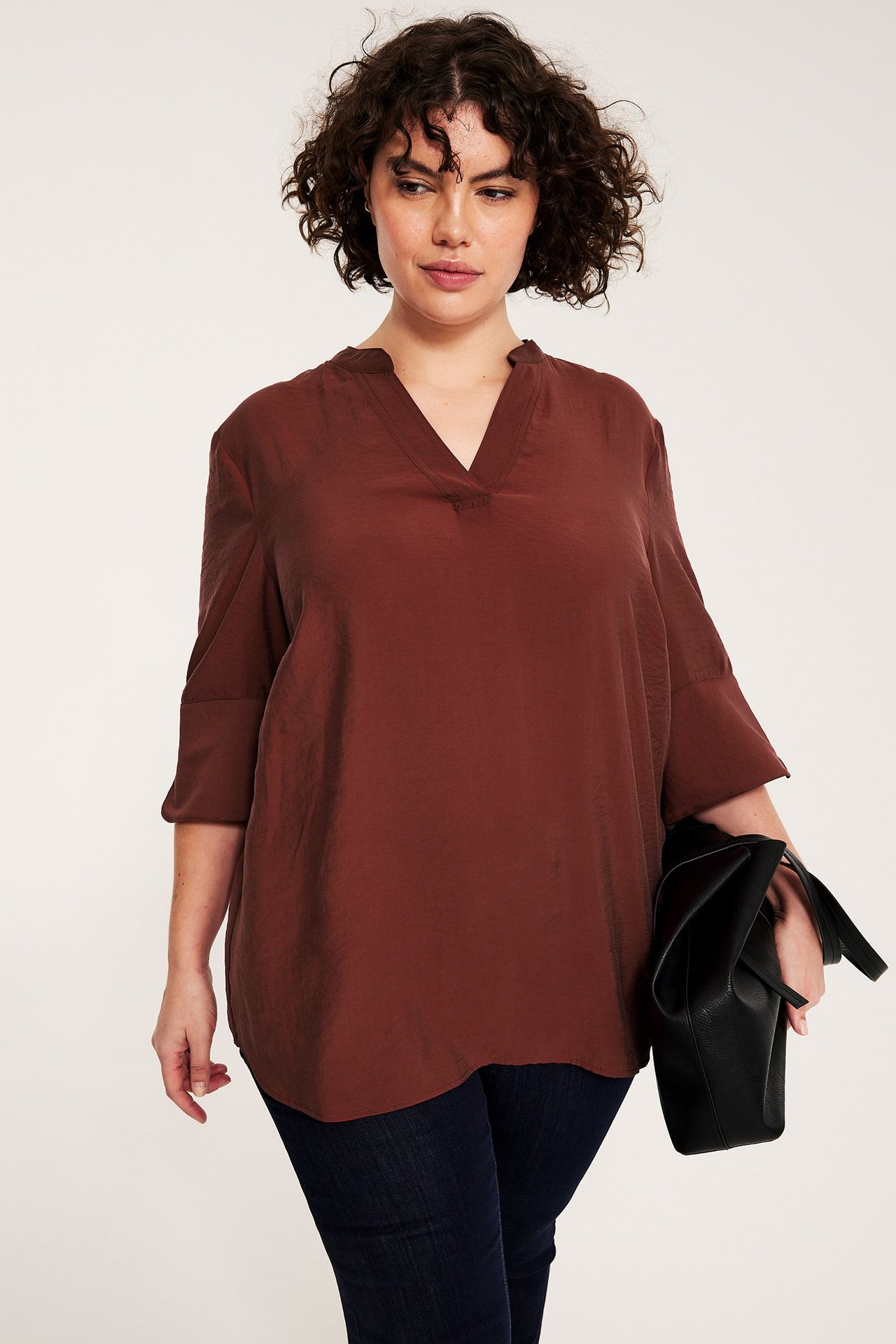 Widok z przodu: Kobieta w luźnej czerwonej jedwabistej bluzce V, ciemnych jeansach, z czarną torebką.