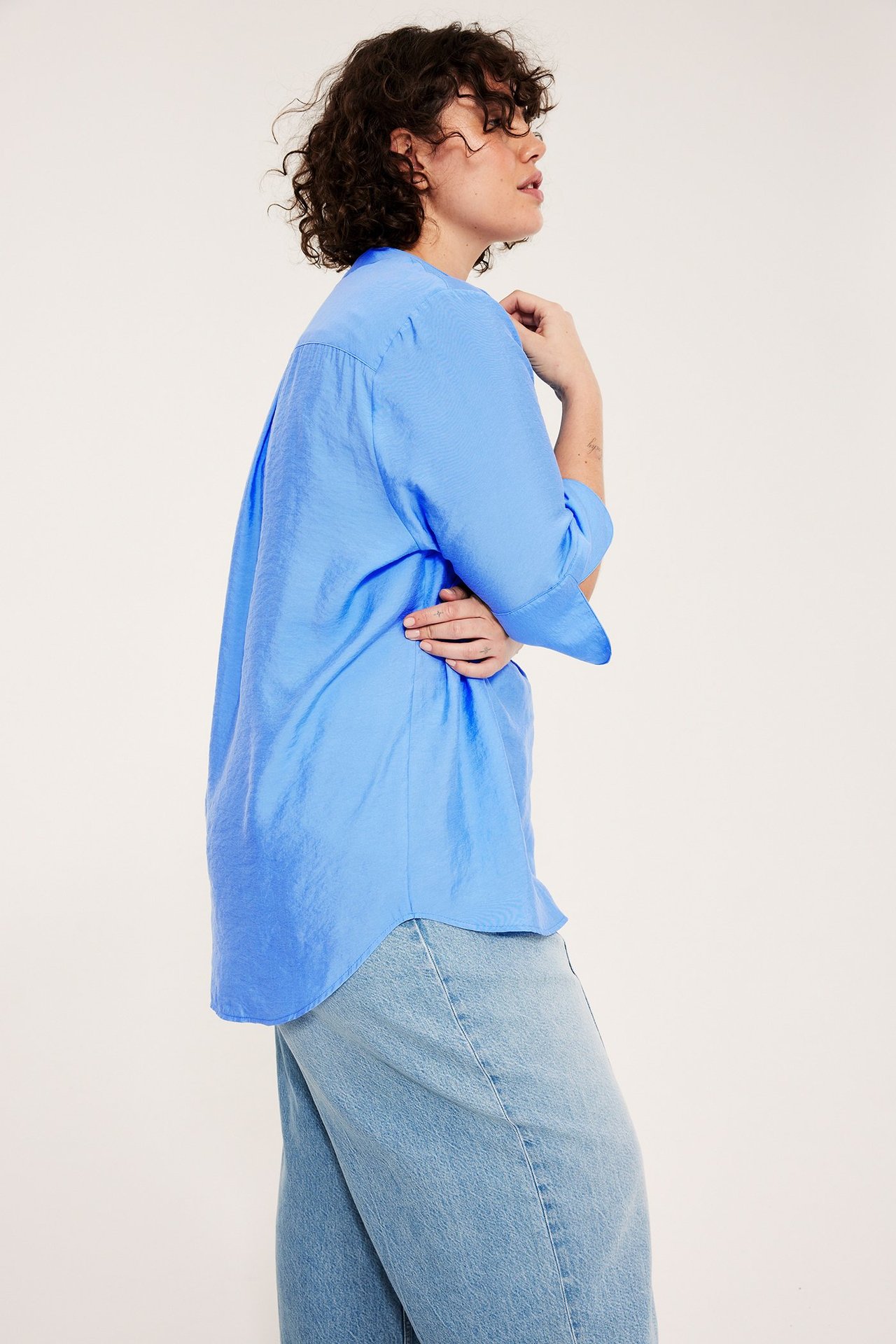 Widok z boku kobiety w luźnej niebieskiej bluzce z V-dekoltem i jasnoniebieskich jeansach.