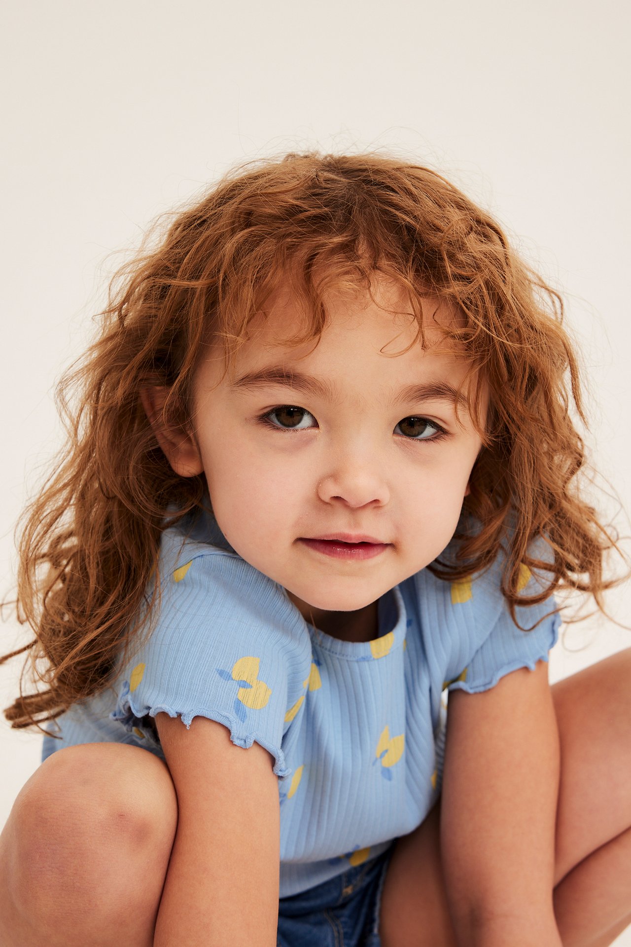 Närbild, framifrån: ett barn i en ljusblå ribbad topp med citrontryck och blå denimshorts.