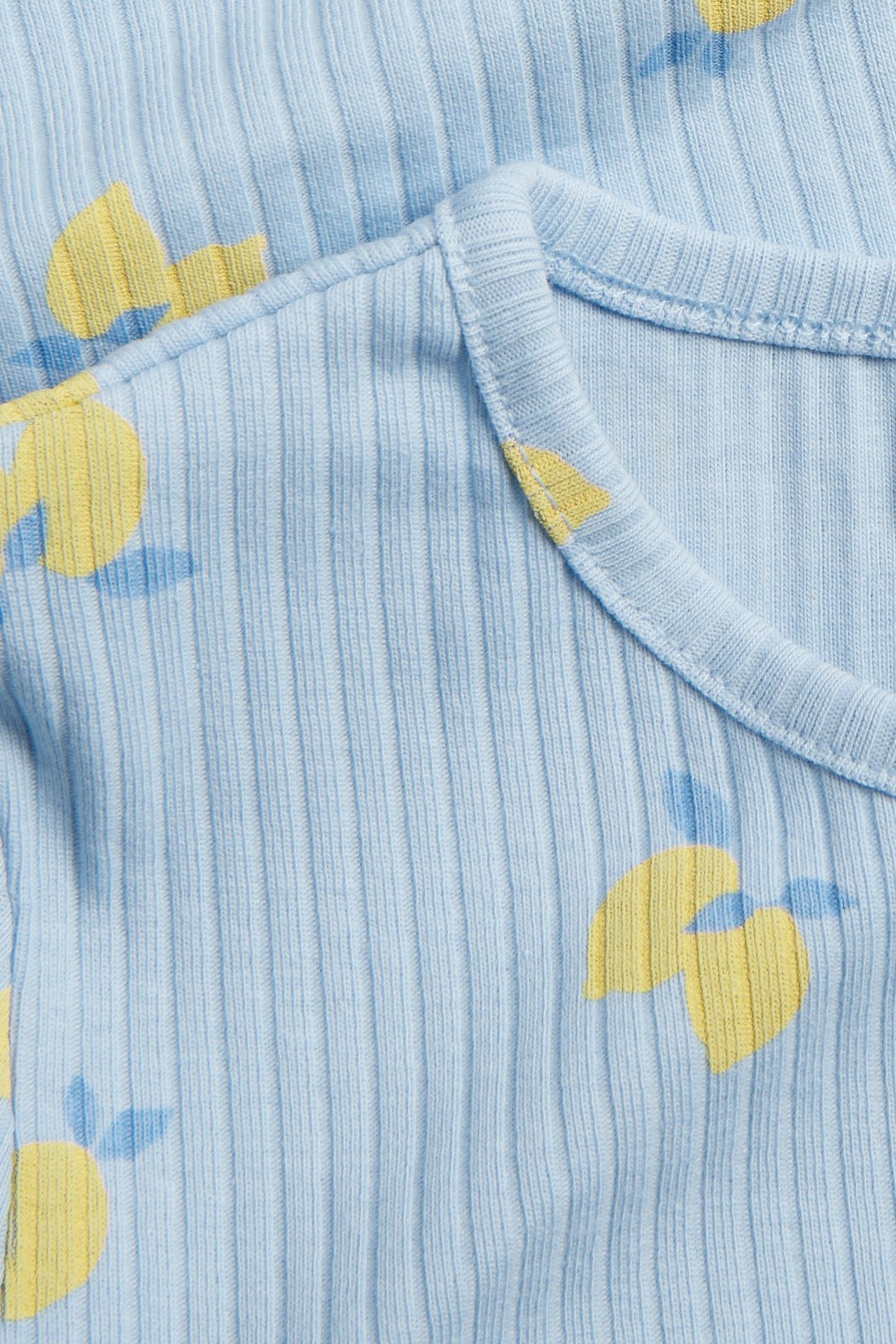 Zbliżenie na jasnoniebieski prążkowany top z żółtym wzorem cytryn i okrągłym dekoltem.