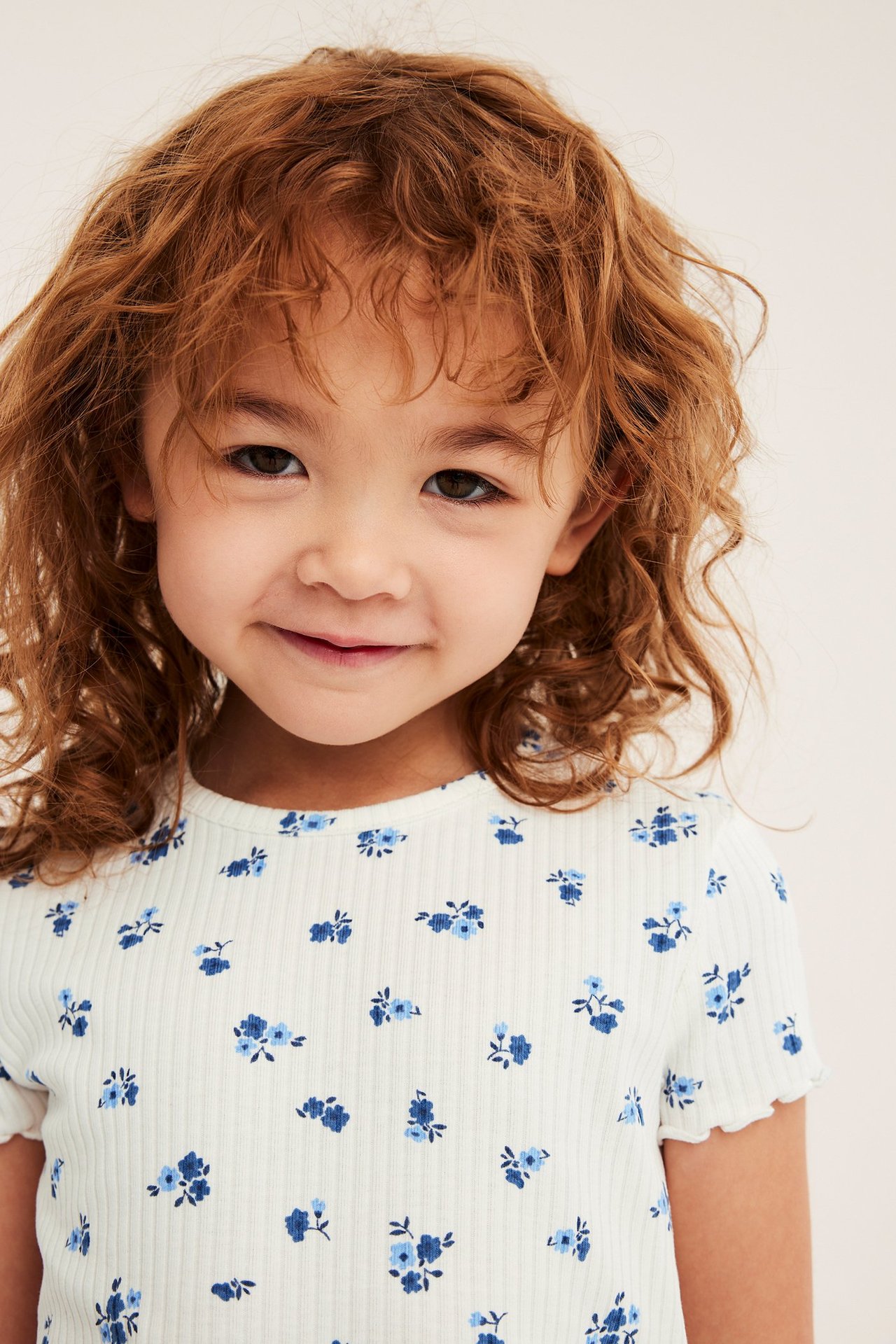Närbild framifrån på ett barn som bär en offwhite ribbad kortärmad topp med blått blommönster.