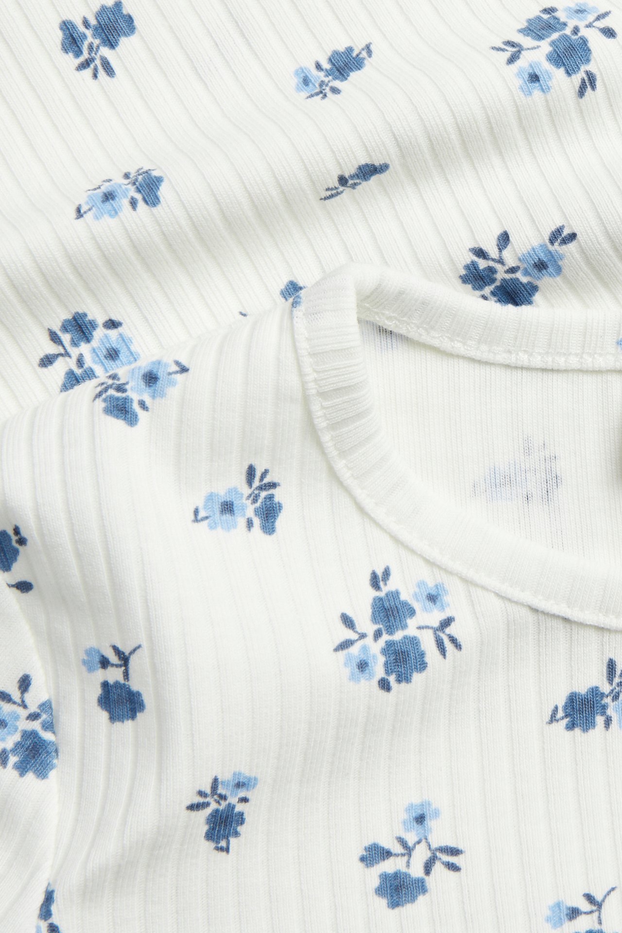 Zbliżenie na kremowy prążkowany bawełniany top w niebieskie kwiaty z przeszyciem typu babylock.