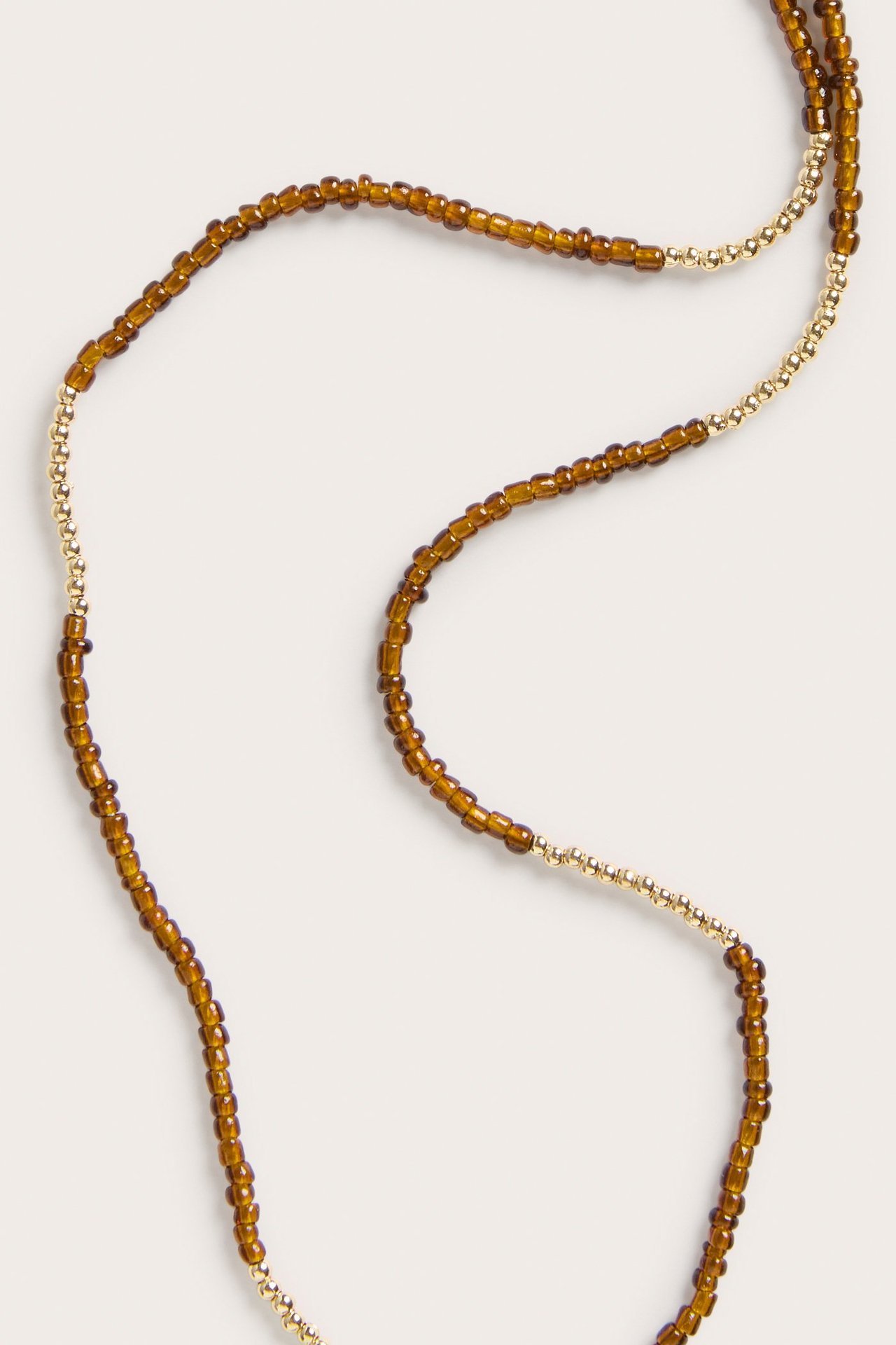 Närbild av ett långt halsband med omväxlande sektioner av små guldfärgade och bärnstensfärgade plastpärlor.