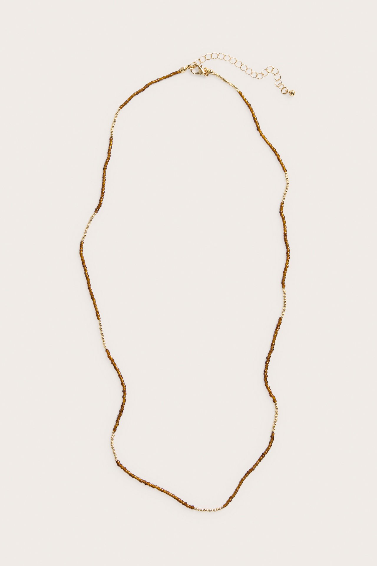 Ovanifrån, ett guldfärgat halsband med små bruna plastpärlor och ett karbinlås.