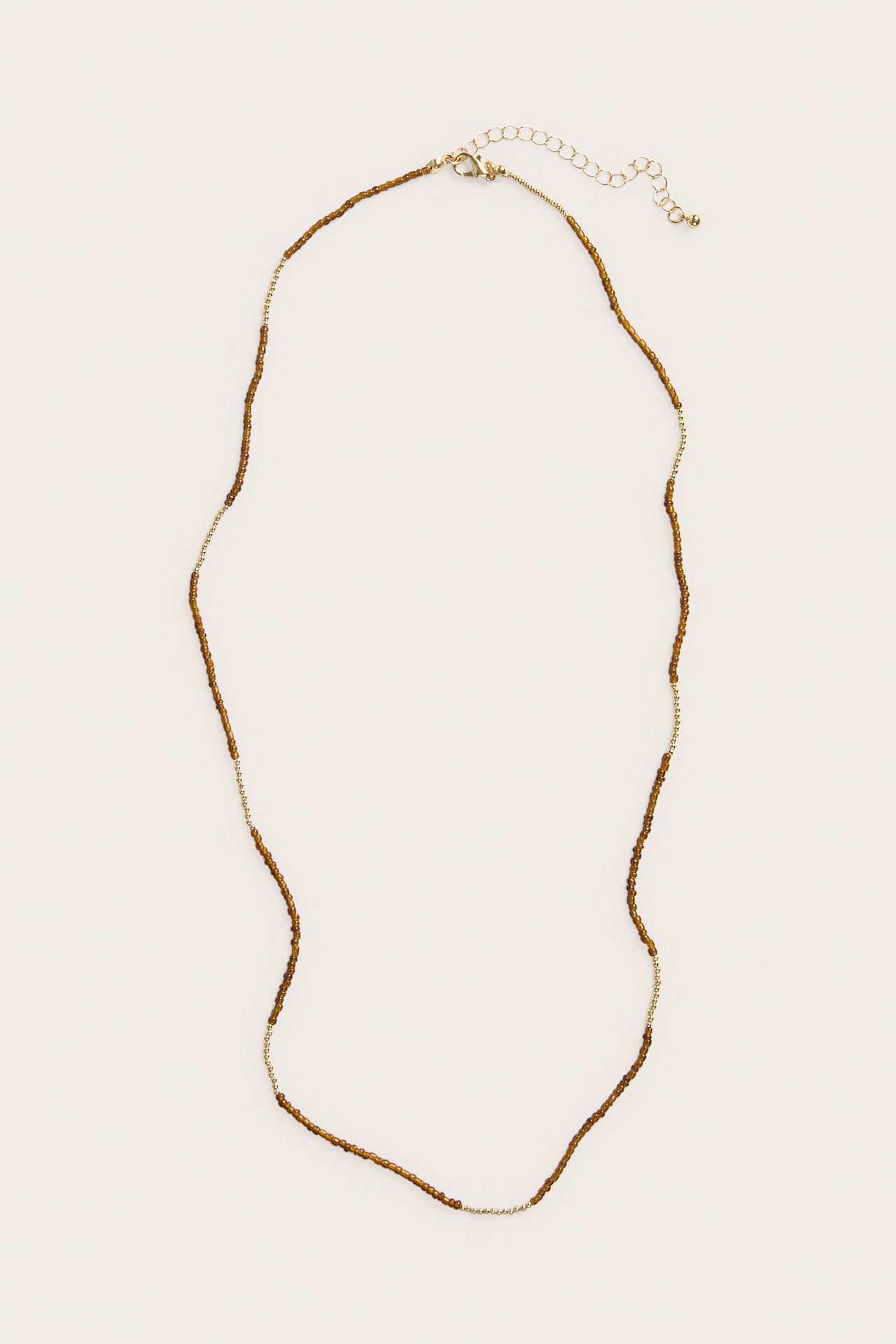 Ovanifrån, ett guldfärgat halsband med små bruna plastpärlor och ett karbinlås.