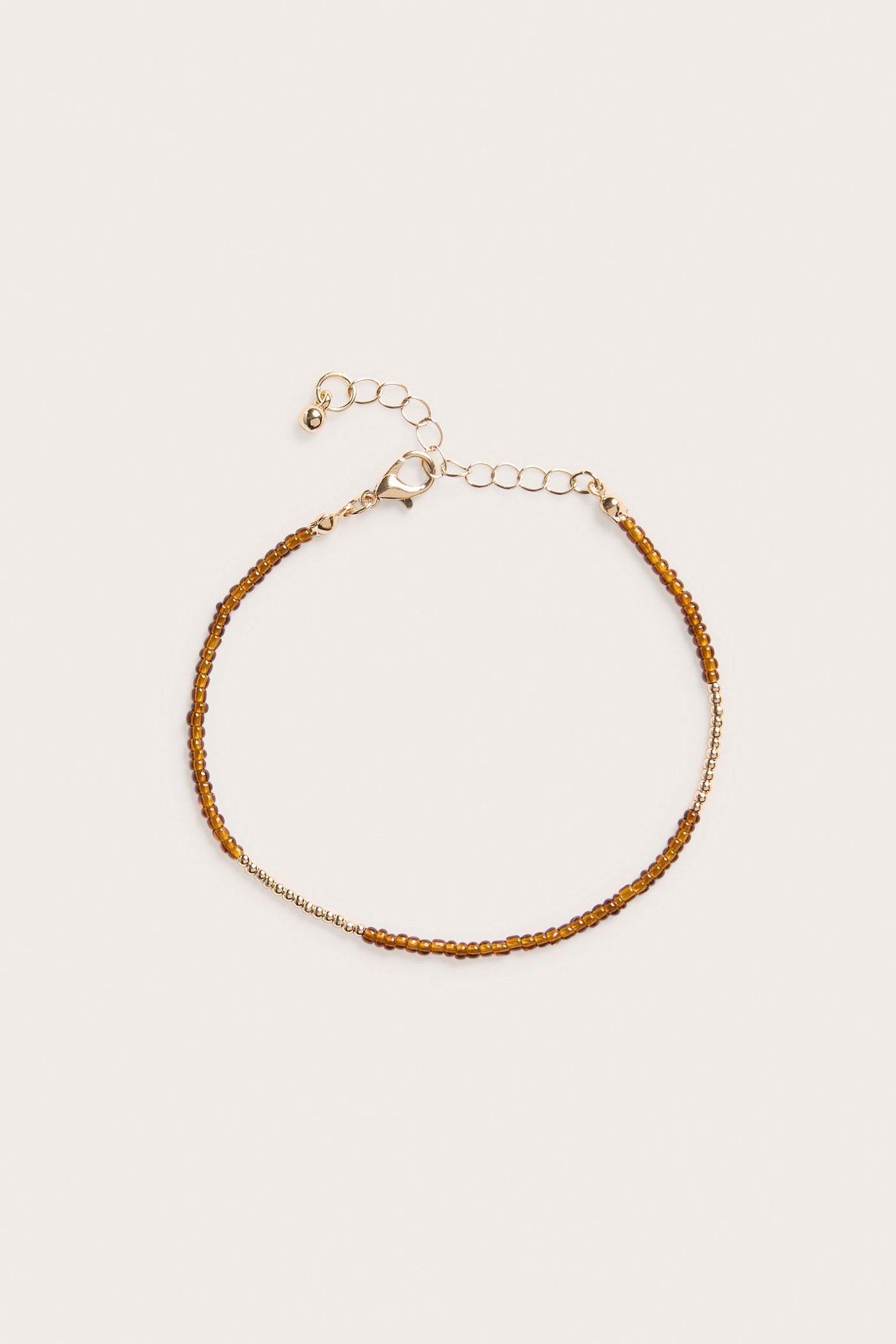 Zbliżenie na złotą bransoletkę z małymi brązowymi plastikowymi koralikami, łańcuszkiem i zapięciem.