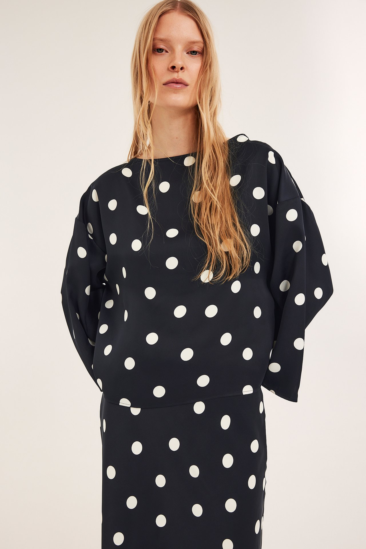 Widok z przodu: Kobieta w czarnej bluzce satynowej w kropki z szerokimi rękawami i pasującej spódnicy.