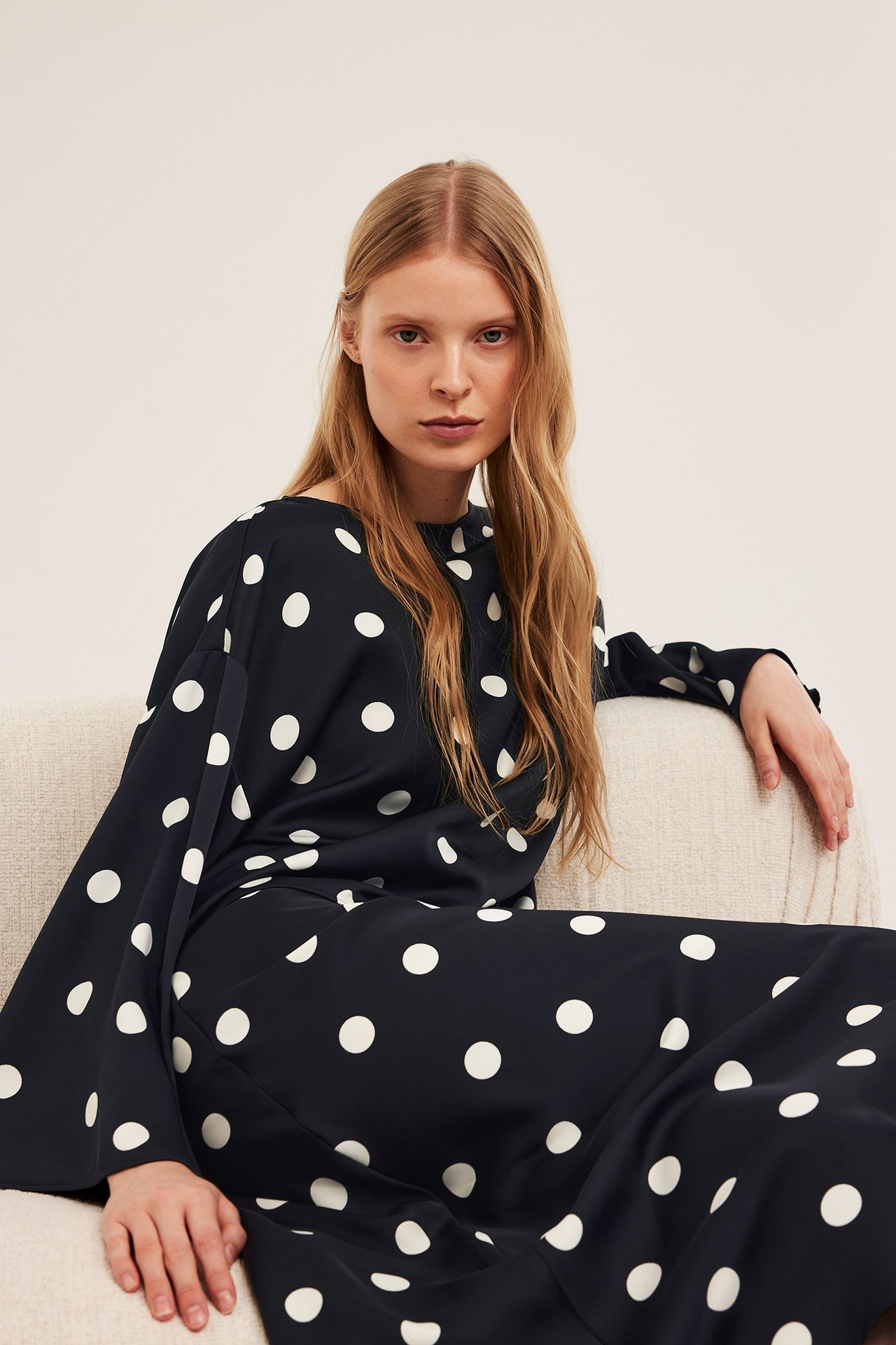 Kobieta w czarnej, satynowej bluzce w kropki z szerokimi rękawami i pasujących spodniach.