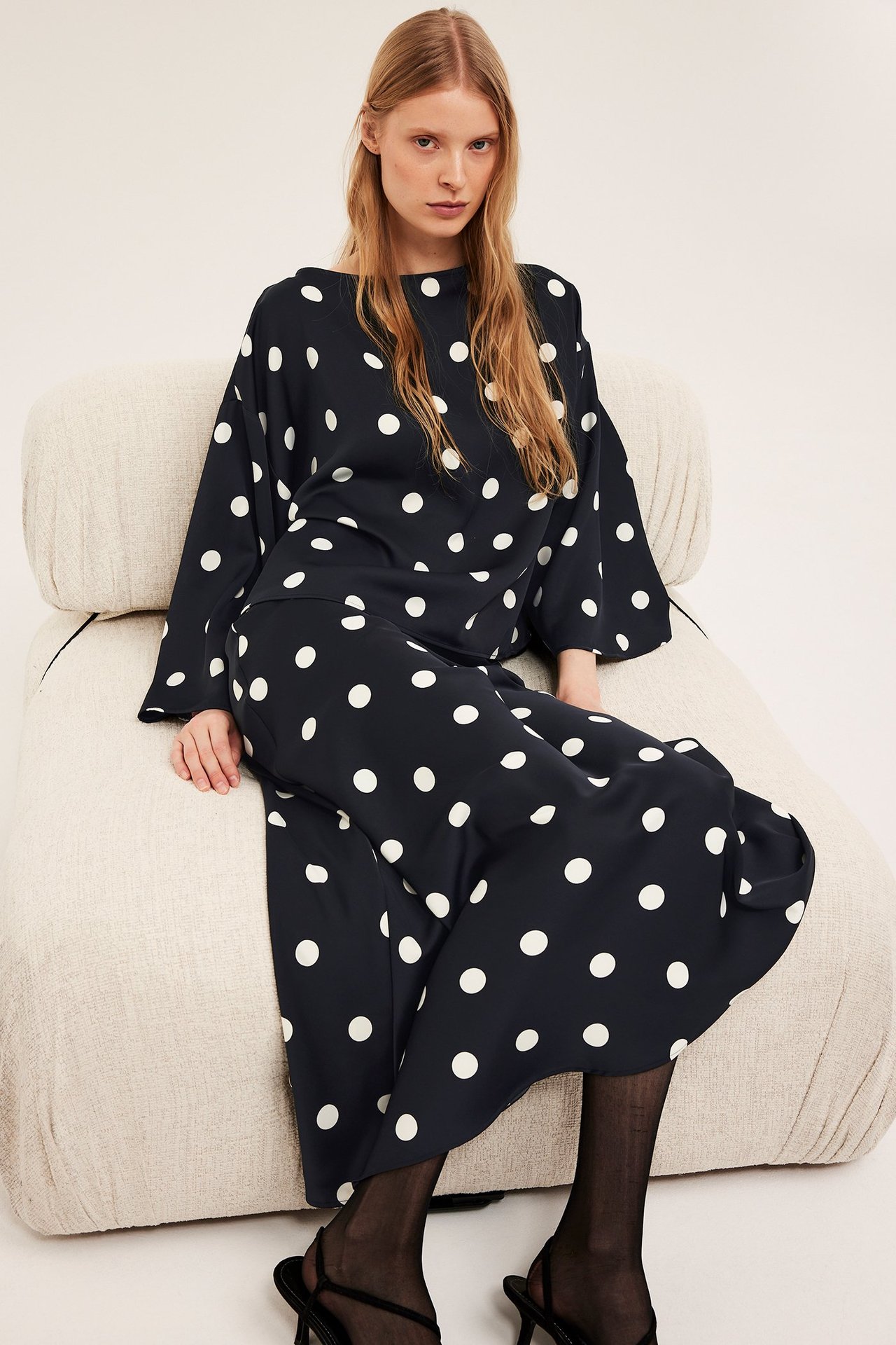 Widok z przodu: kobieta w czarnej bluzce satynowej w kropki z szerokimi rękawami i pasującej spódnicy.