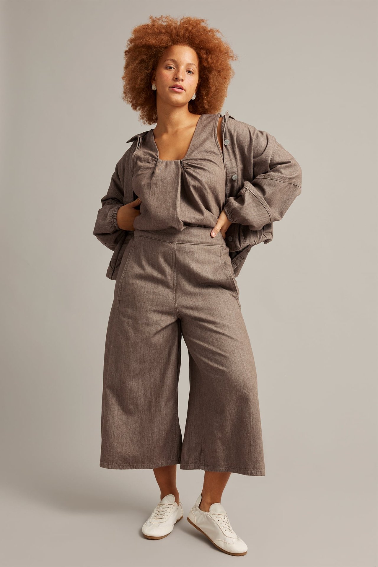 Frontalvisning av en kvinne i brune melange pull-on culottejeans, matchende topp, jakke og hvite joggesko.