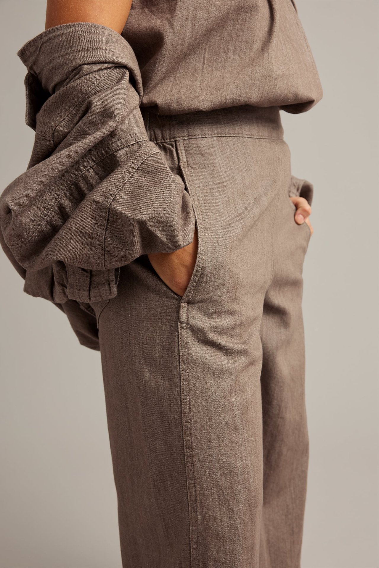 Nærbilde, side: kvinne i brune melange pull-on culotte-jeans av bomull, matchende topp, hånd i lommen.