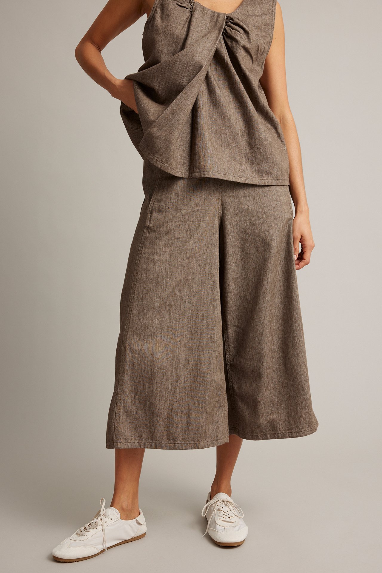 Nainen ruskeassa hihattomassa toppi- ja culottes-setissä, edestä päin, valkoisissa lenkkareissa.