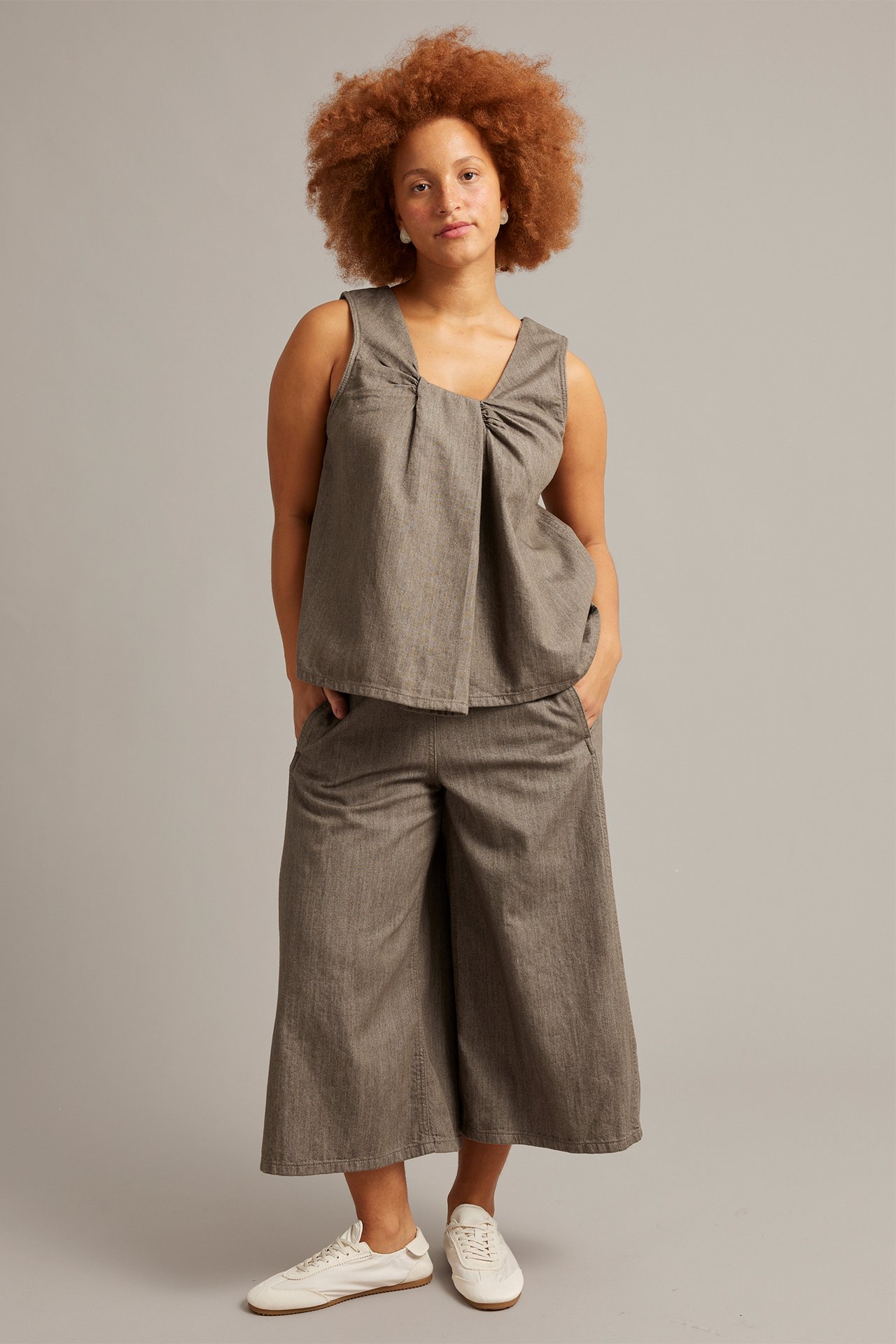Front view: Kvinna i brunmelerad denimtopp med omlottsringning, matchande culottes och vita sneakers.