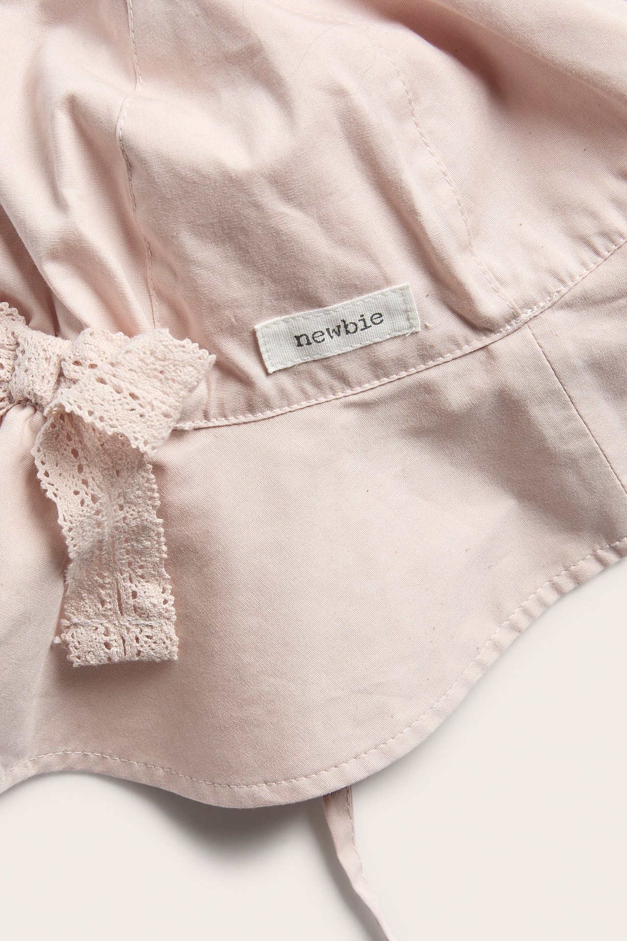 Zbliżenie na jasnoróżowy bawełniany kapelusz przeciwsłoneczny z dłuższym tyłem, wiązaniami i ozdobną koronkową kokardką.