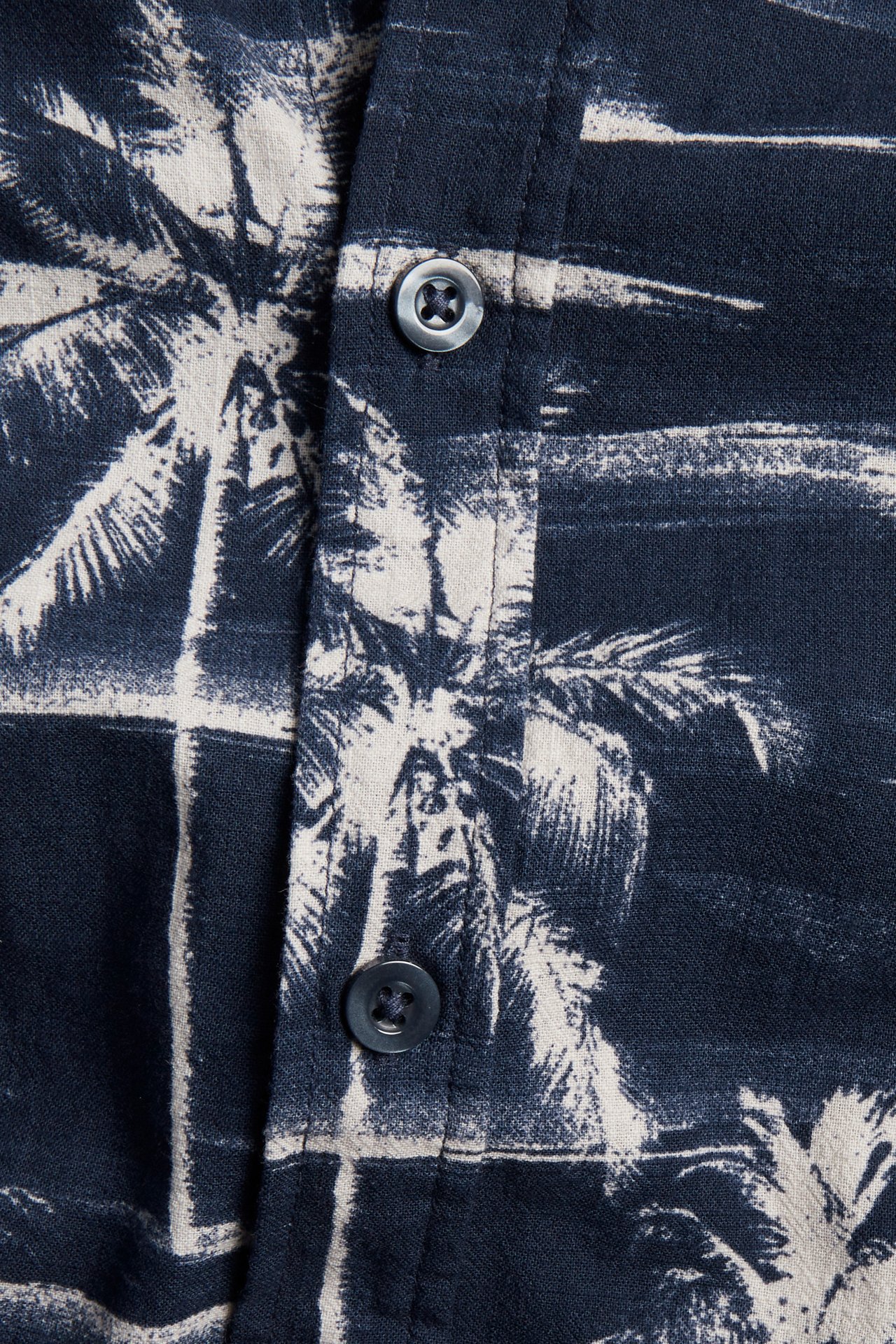 Närbild av en mörkblå kortärmad herrskjorta i bomull med vitt palmträdsmönster och synliga knappar.