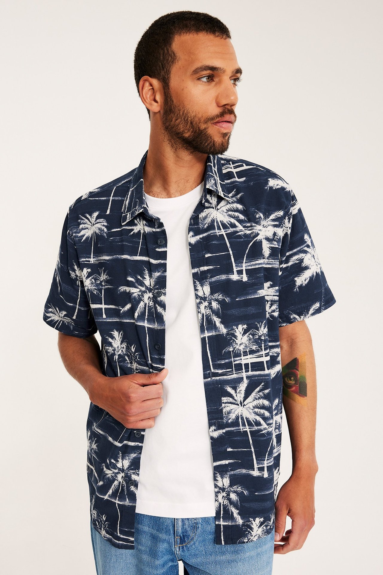 Framifrån: man i mörkblå kortärmad skjorta med palmträdsmönster, öppen över en vit t-shirt.