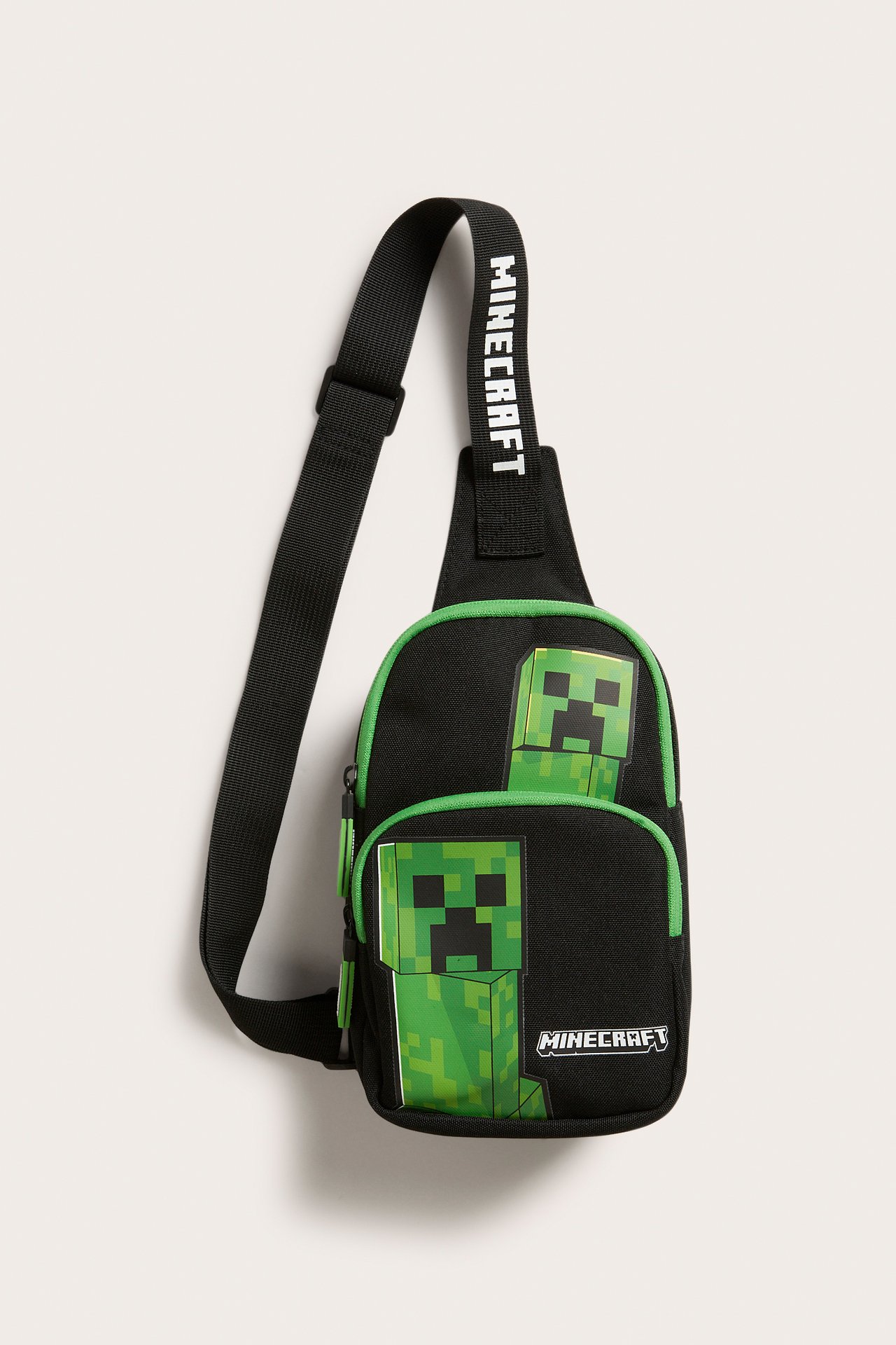 Edestä: musta poikkivartalolaukku vihreällä reunuksella, Minecraft Creeper -kuviolla ja säädettävällä hihnalla.
