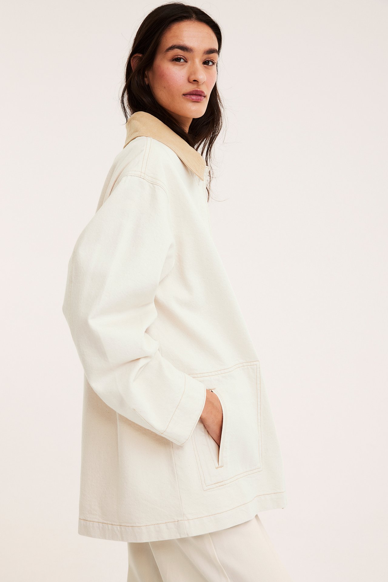 Widok z boku kobiety w beżowej kurtce twillowej z kołnierzem sztruksowym i pasującymi beżowymi spodniami.