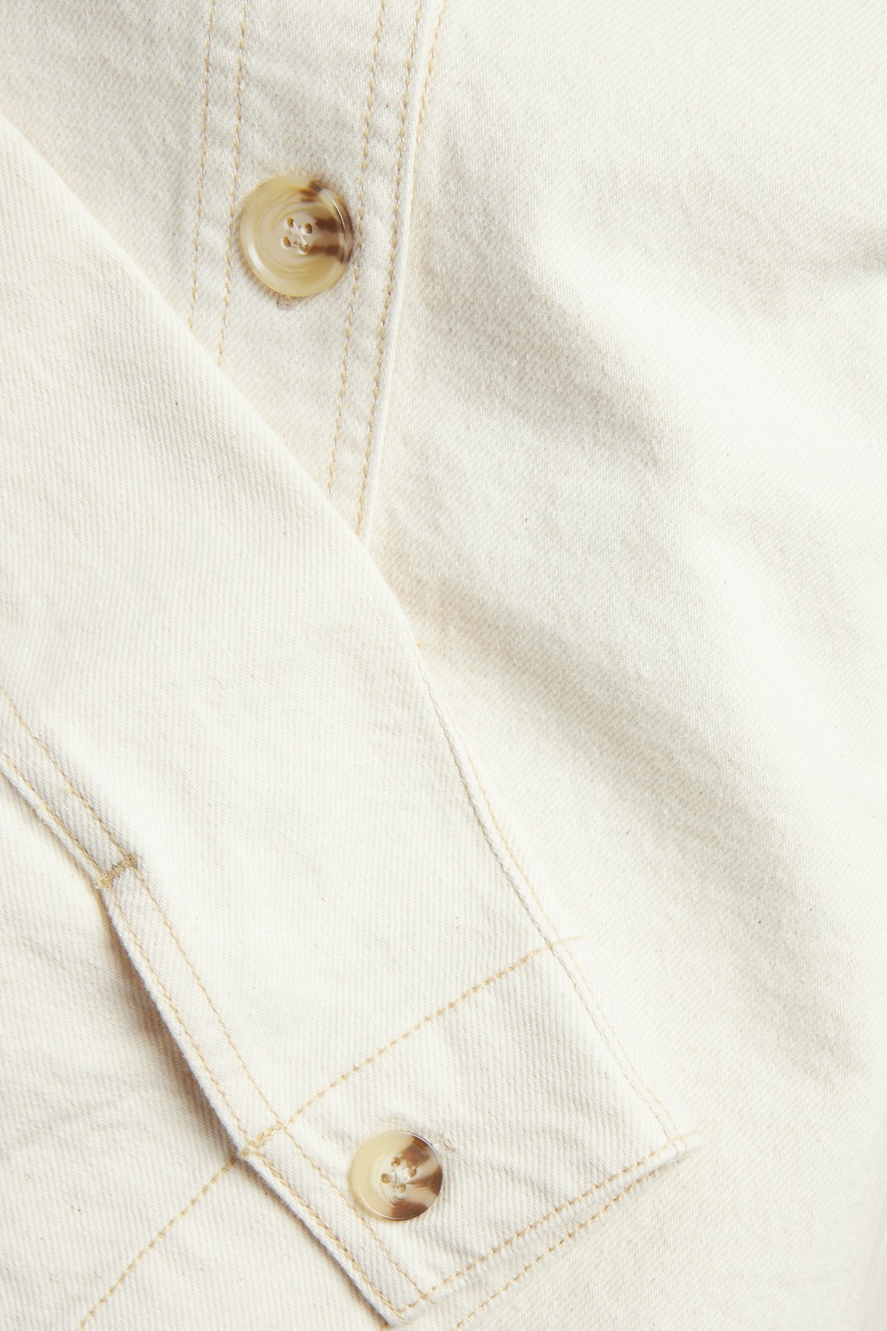 Närbild av en beige twillskjortjacka med kontrastsömmar och marmorerade knappar.