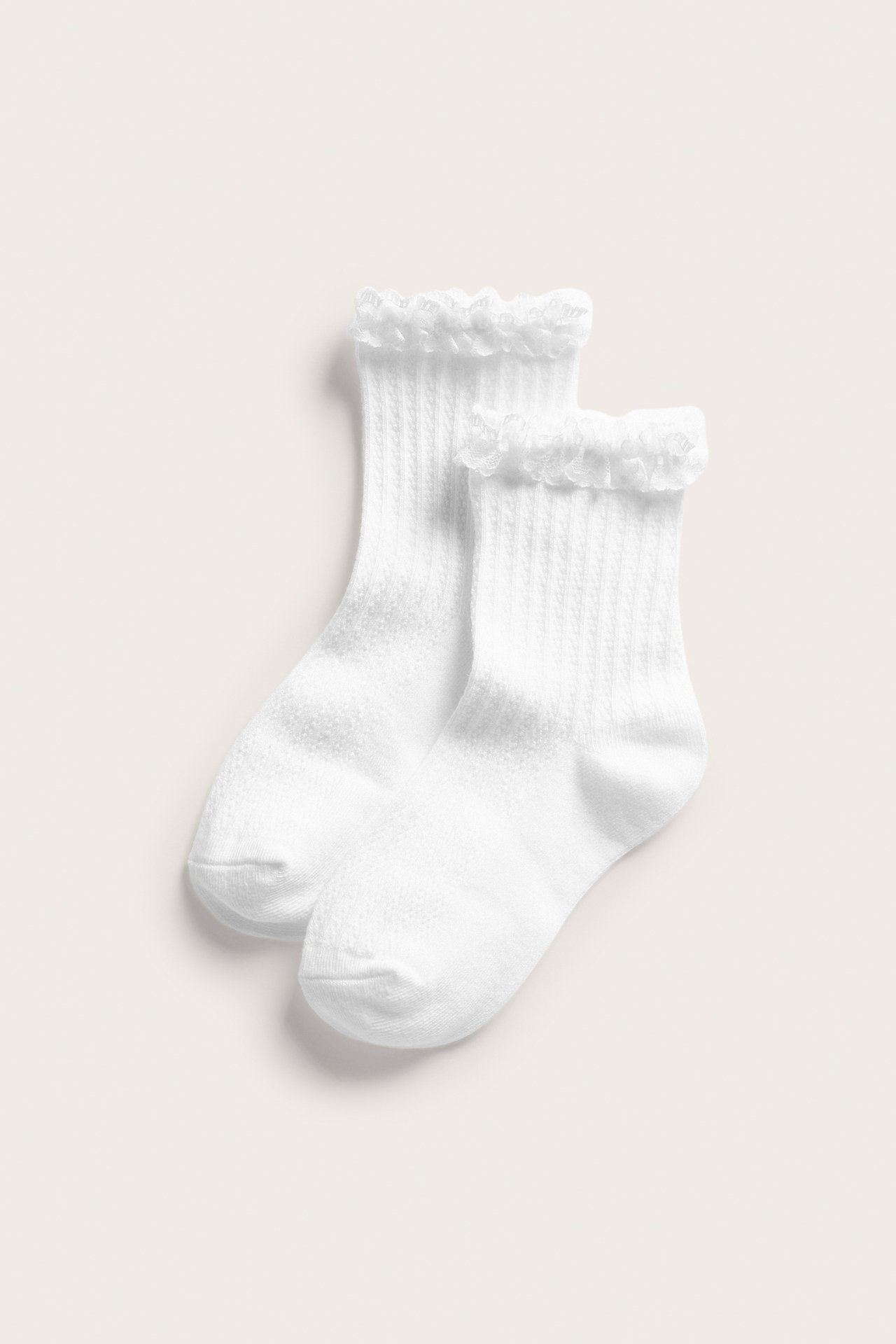 Edestäpäin, kaksi paria valkoisia ribbineulottuja sukkia, joissa on röyhelöreuna resorin kohdalla.