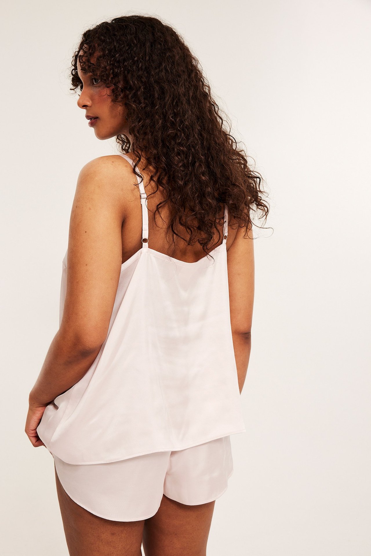 Bakifrån, kvinna i rosa satinpyjamas med reglerbara axelband.