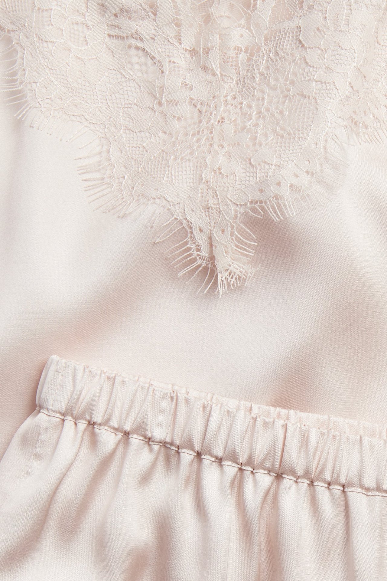 Närbild: Rosa satinpyjamas med spetsdetaljer i halsringningen och matchande shorts med resår i midjan.