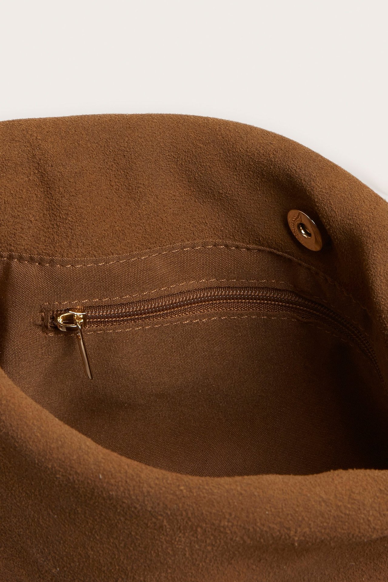 Lähikuva vaaleanruskean mokkanahkaisen käsilaukun sisäosasta, vetoketjullinen tasku ja magneettineppari.