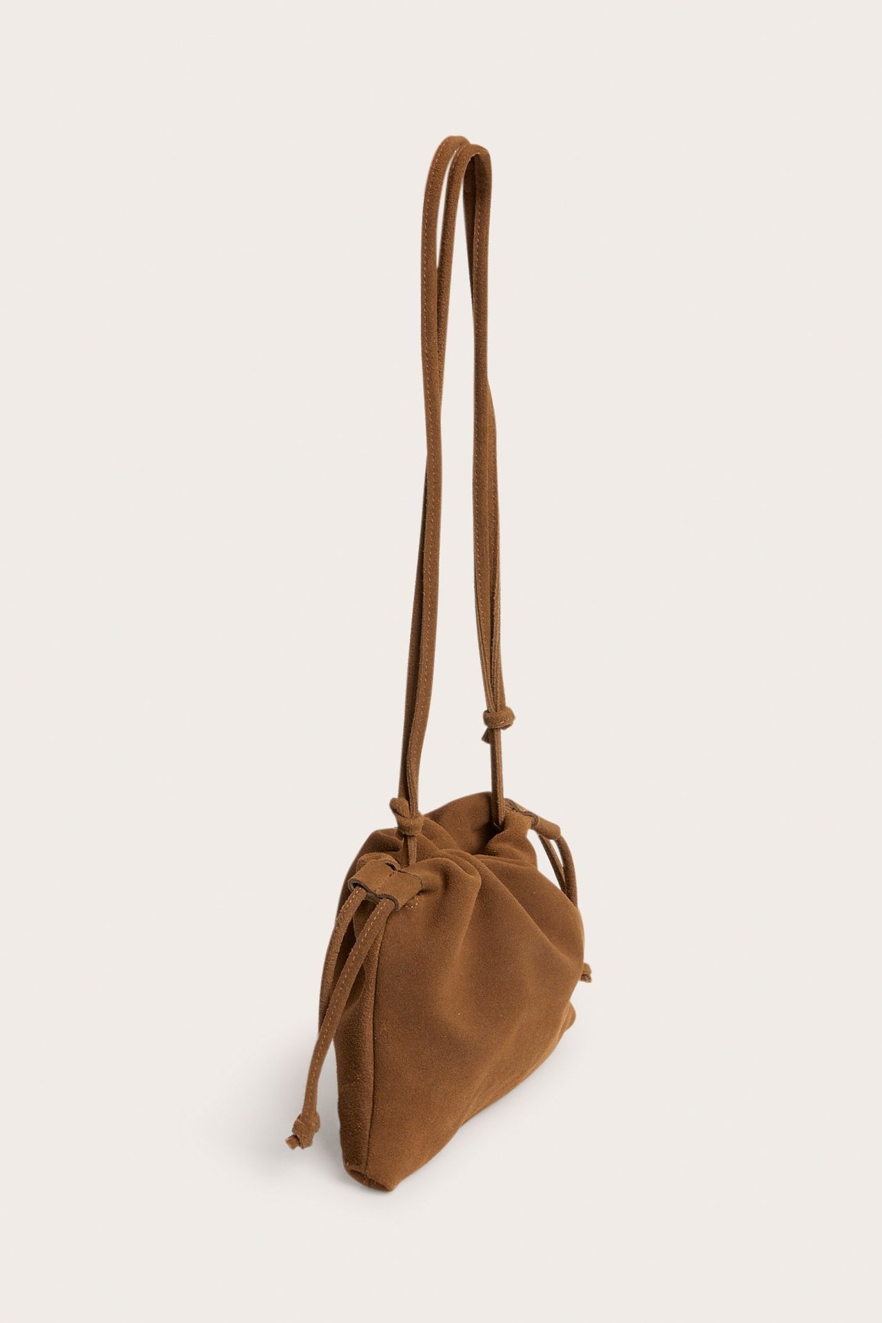 Jasnobrązowa zamszowa torebka-worek ze ściągaczem i regulowanym paskiem, widok z boku.