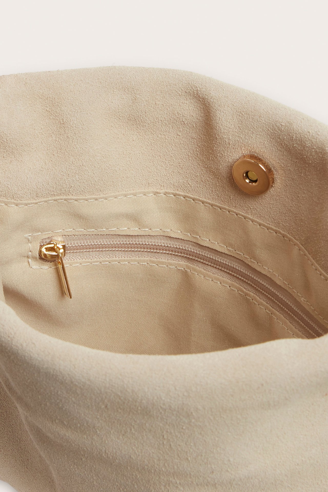 Lähikuva beigen mokkanahkaisen käsilaukun sisältä, näyttää vetoketjullisen sisätaskun ja magneettinepparikiinnityksen.