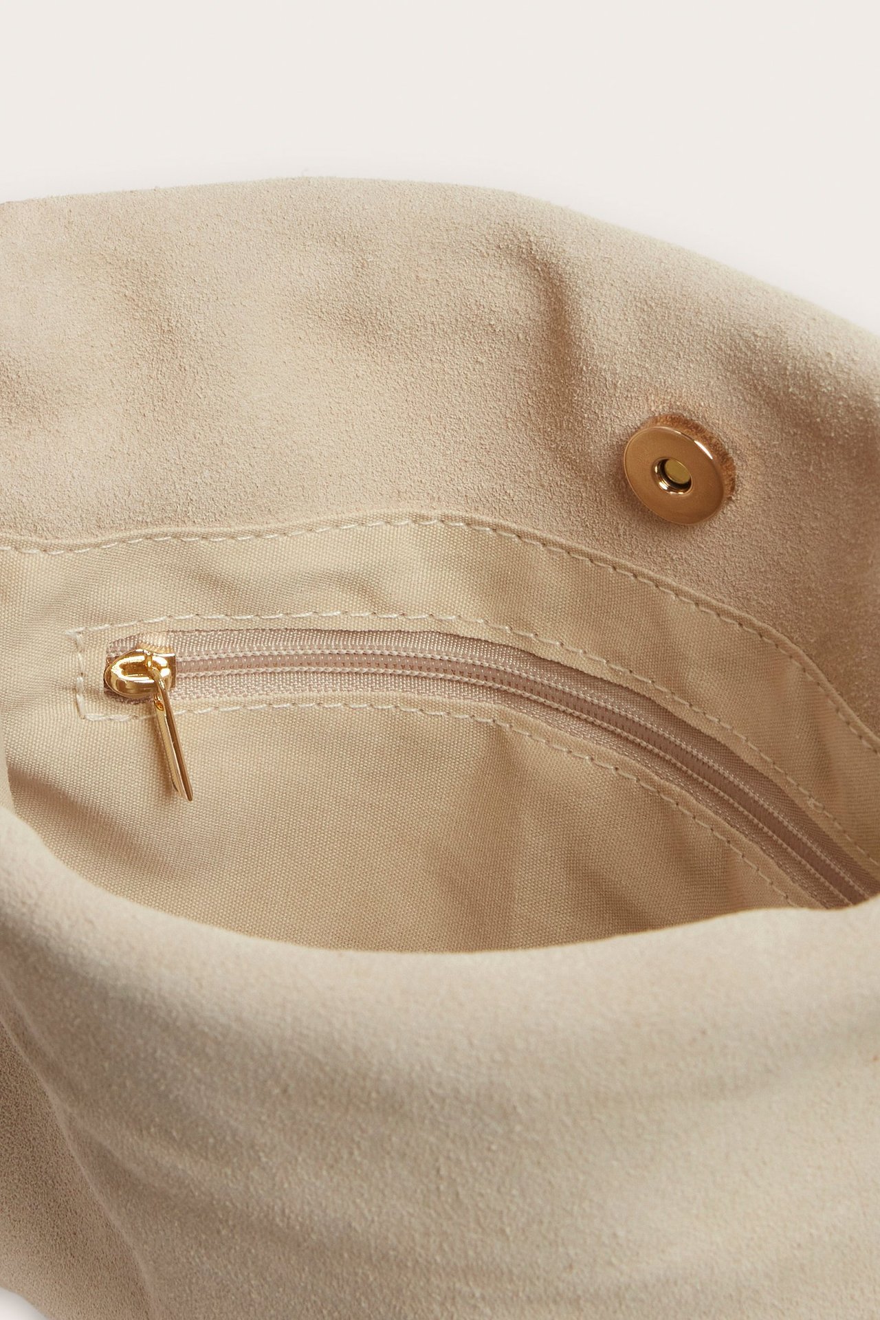 Zbliżenie wnętrza beżowej zamszowej torebki, ukazujące wewnętrzną kieszeń na suwak i magnetyczne zapięcie.