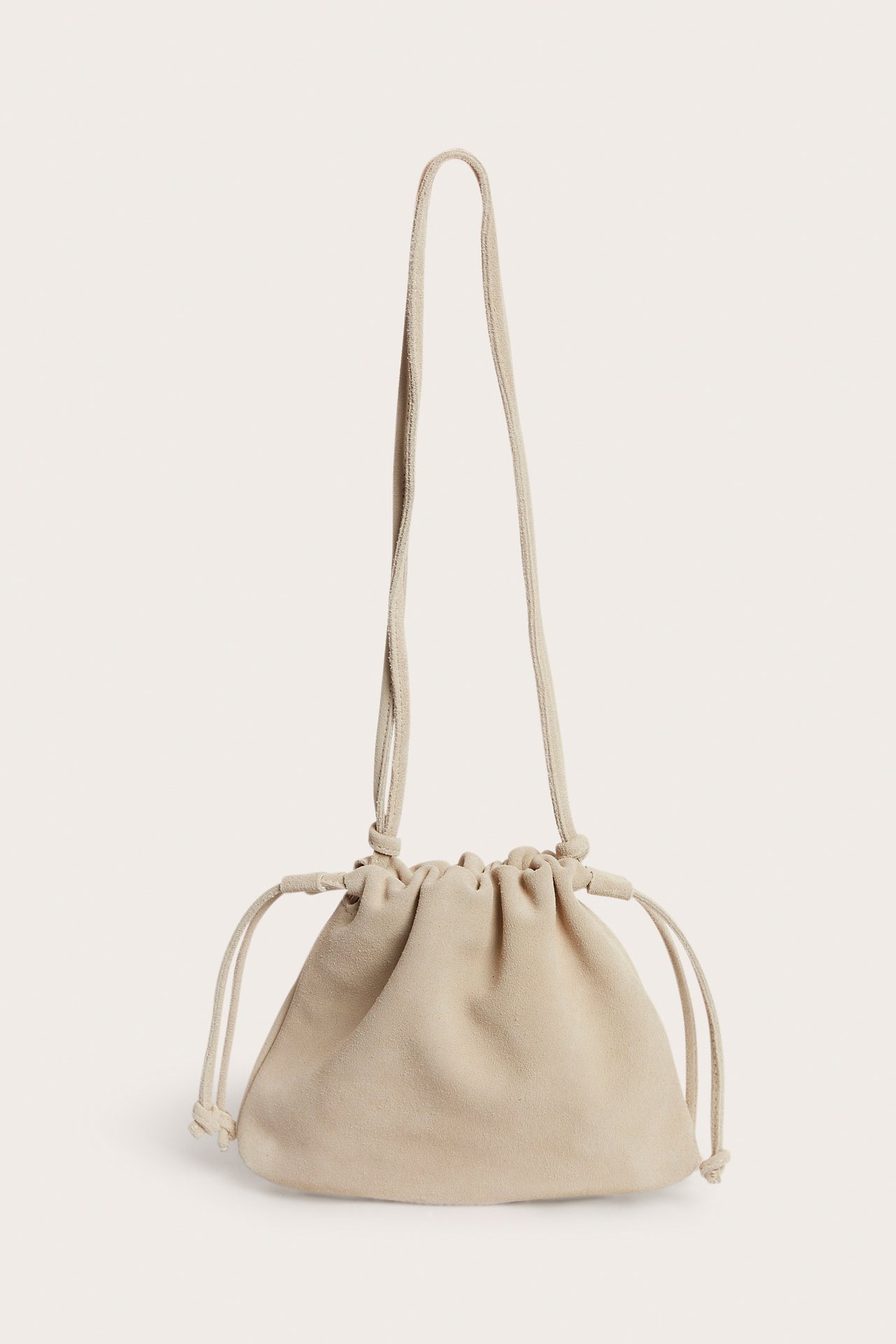 Edestä, beige mokkanahkainen nyöripussukkakäsilaukku pitkällä säädettävällä olkahihnalla.