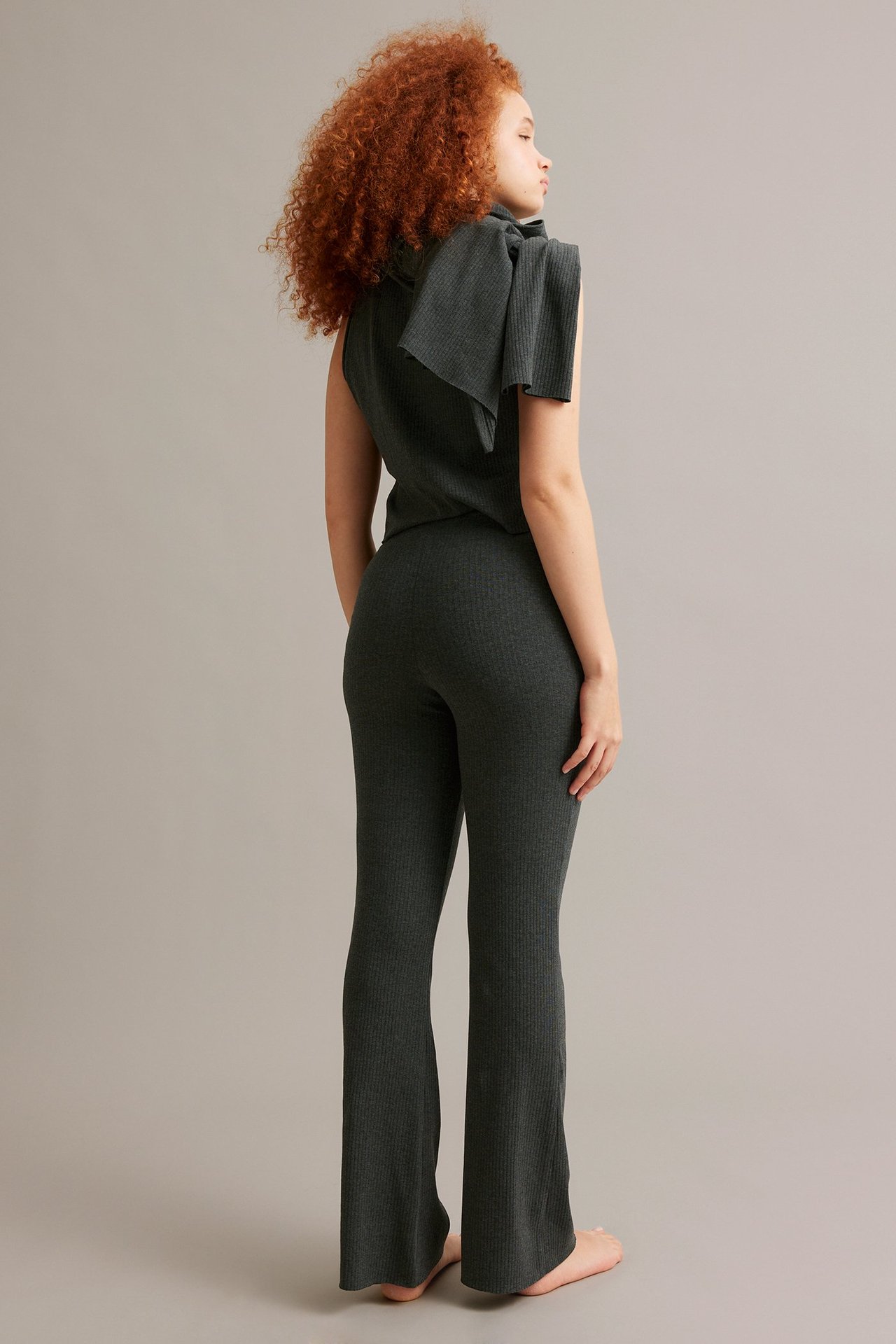 Sida vy av en kvinna som bär mörkgrå ribbade bootcut-byxor med matchande ribbad ärmlös topp.