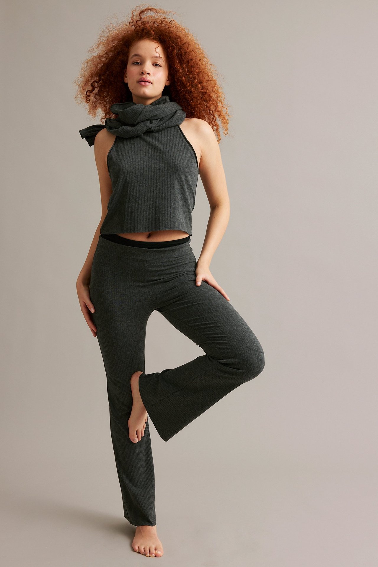 Framifrån: Kvinna i antracitmelerade ribbade bootcut byxor, matchande ribbad crop top och halsduk.