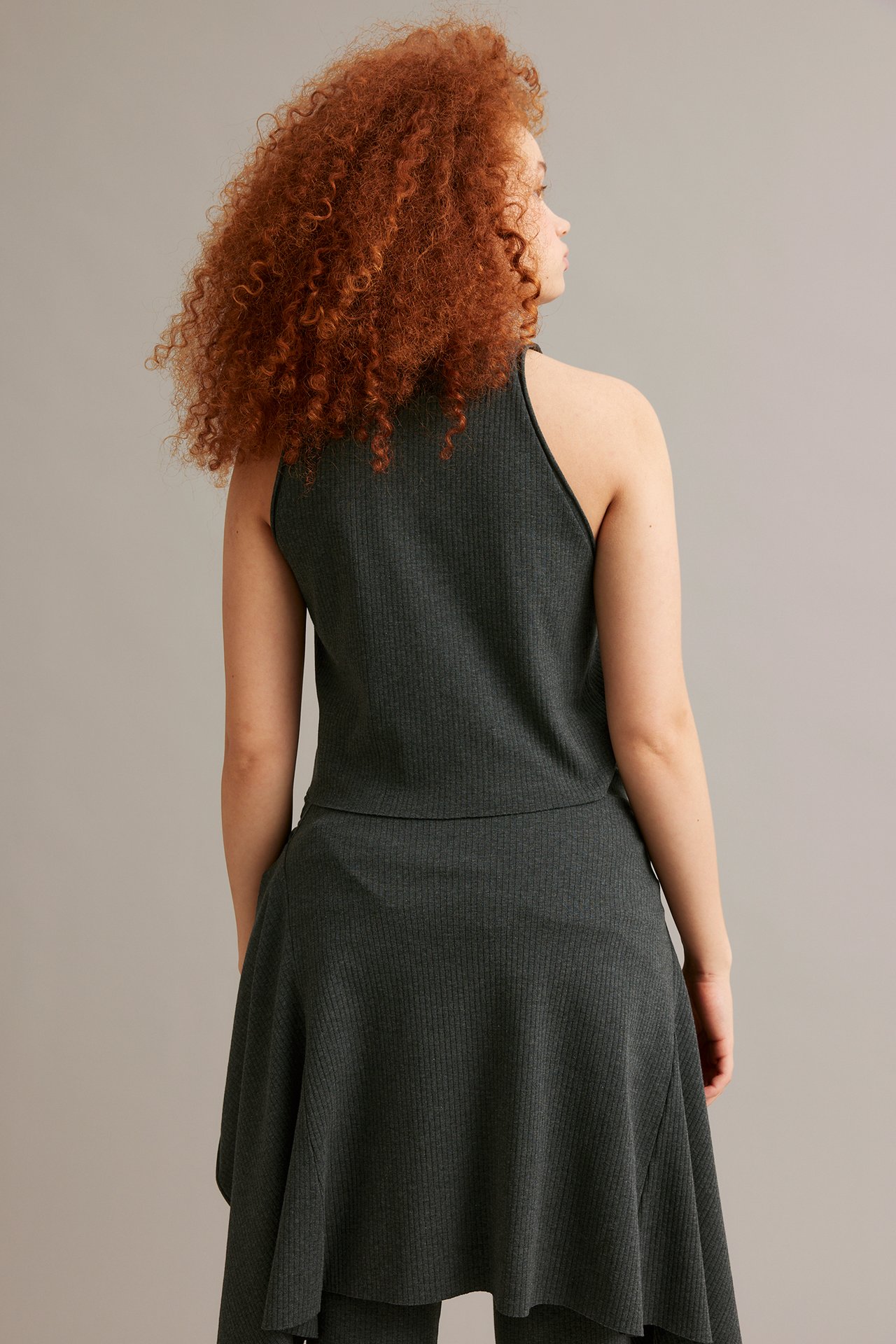 Ryggutsikt av en kvinne i antrasittfarget melert ribbet singlet og matchende ribbet utsvingt skjørt.