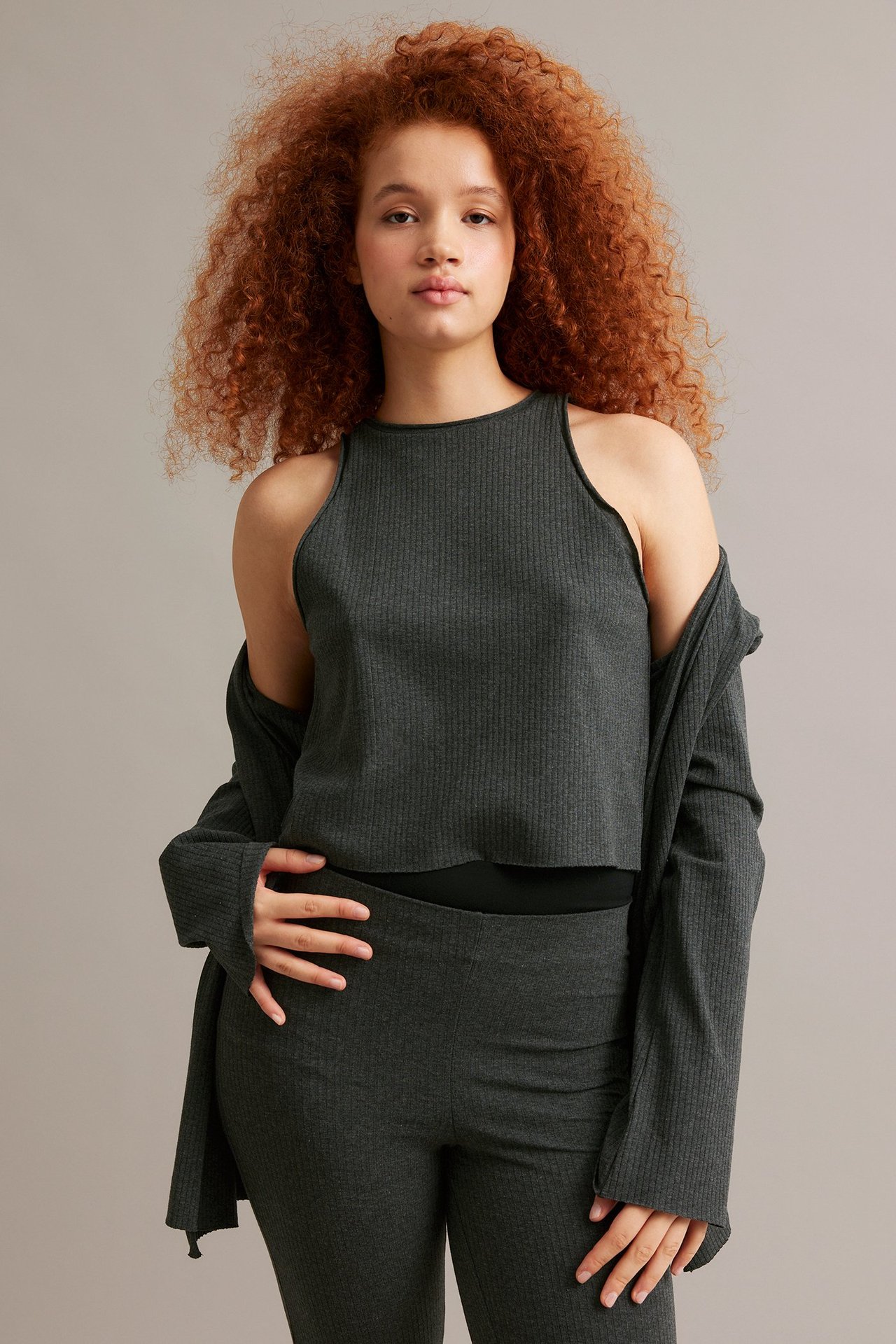 Frontvy av kvinna i mörkgrått ribbat linne, matchande öppen kofta och byxor.