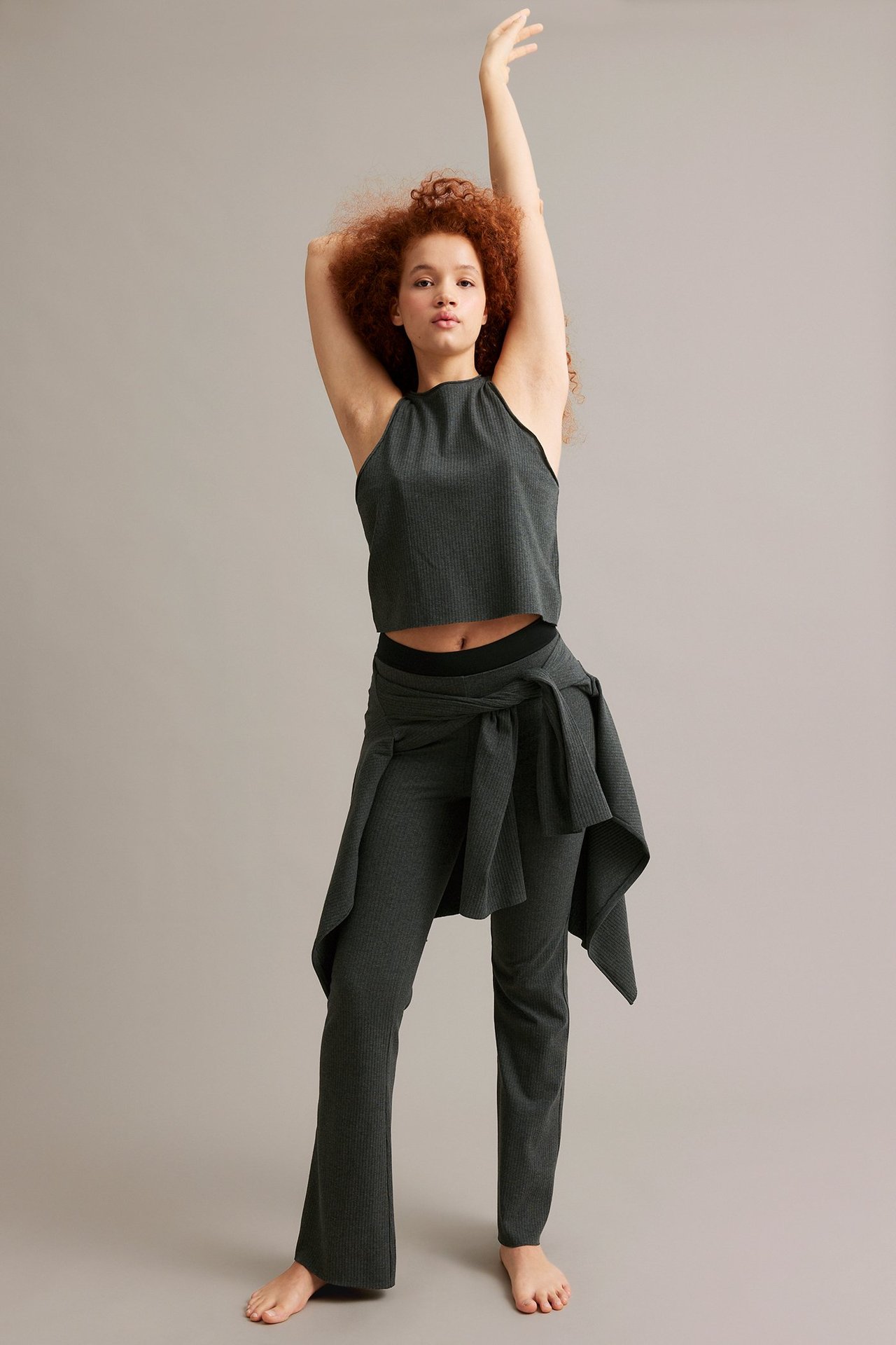 Forfra: kvinne i antrasittfarget ribbet kort topp, matchende bukser og knyttet genser rundt livet.