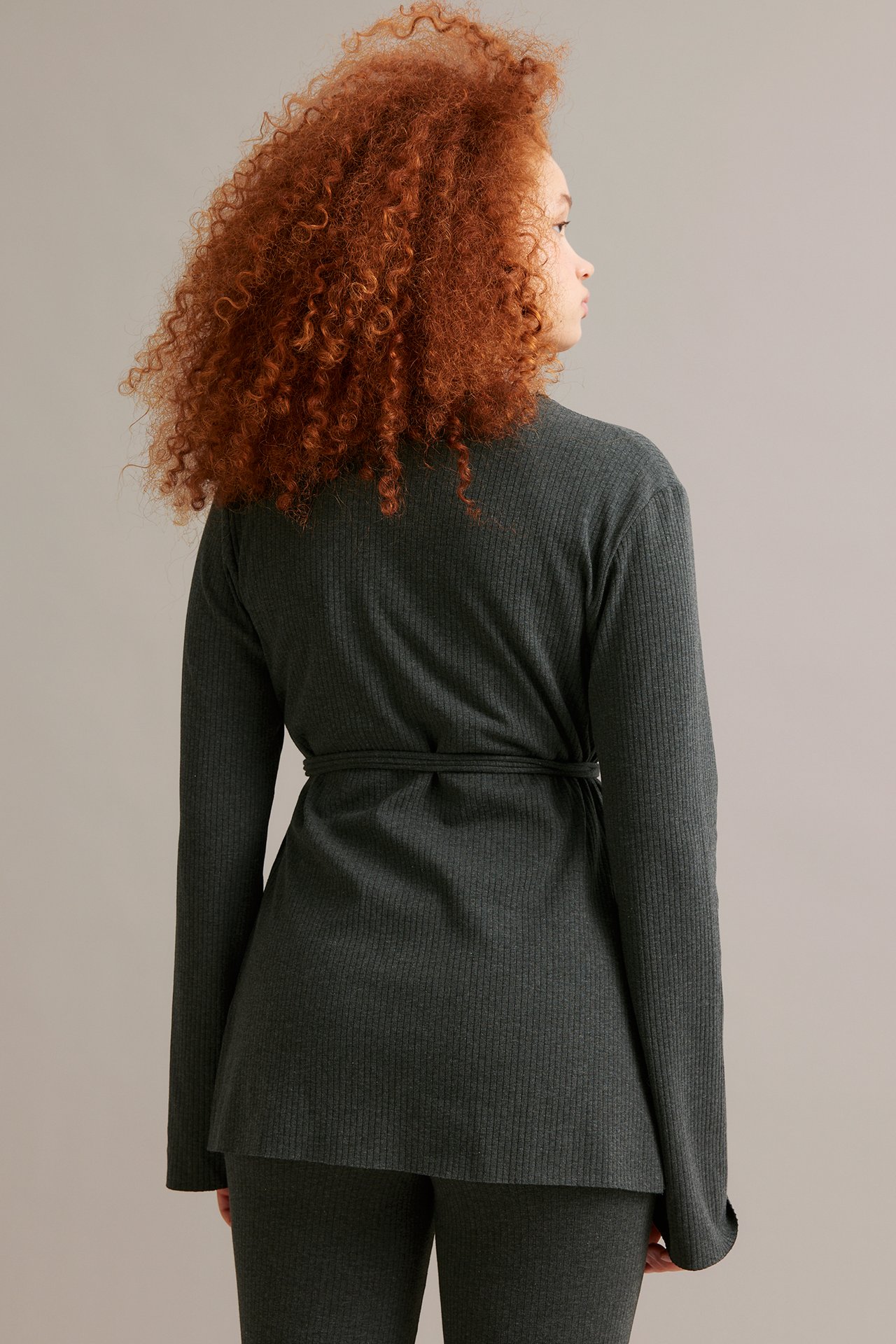 Widok z tyłu: kobieta w ciemnoszarym melanżowym prążkowanym kardiganie, wiązanym, z pasującymi spodniami.
