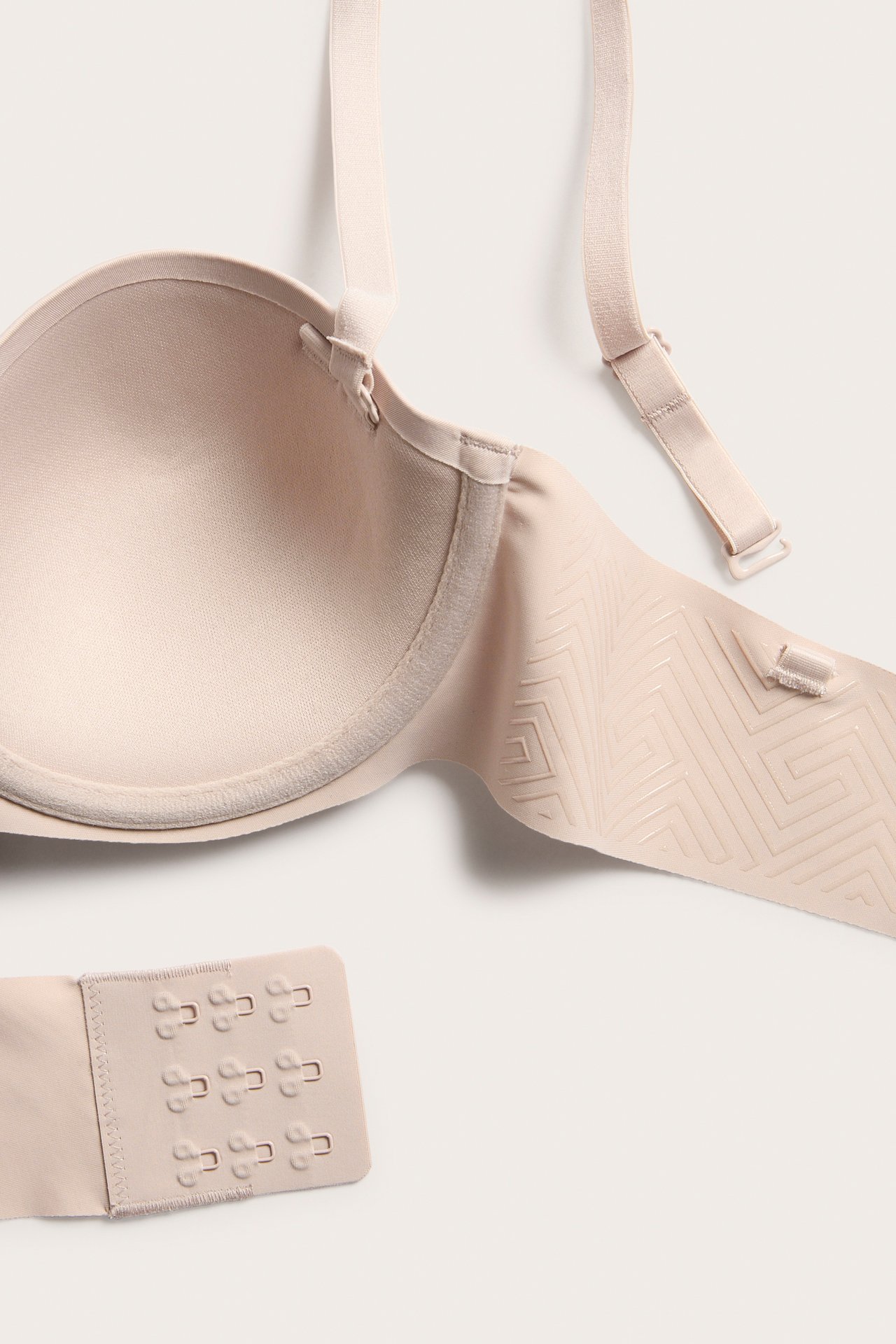 Zbliżenie na jasnoróżowy biustonosz balconette z odpinanymi ramiączkami, wzorzystym paskiem i zapięciem na haftki.