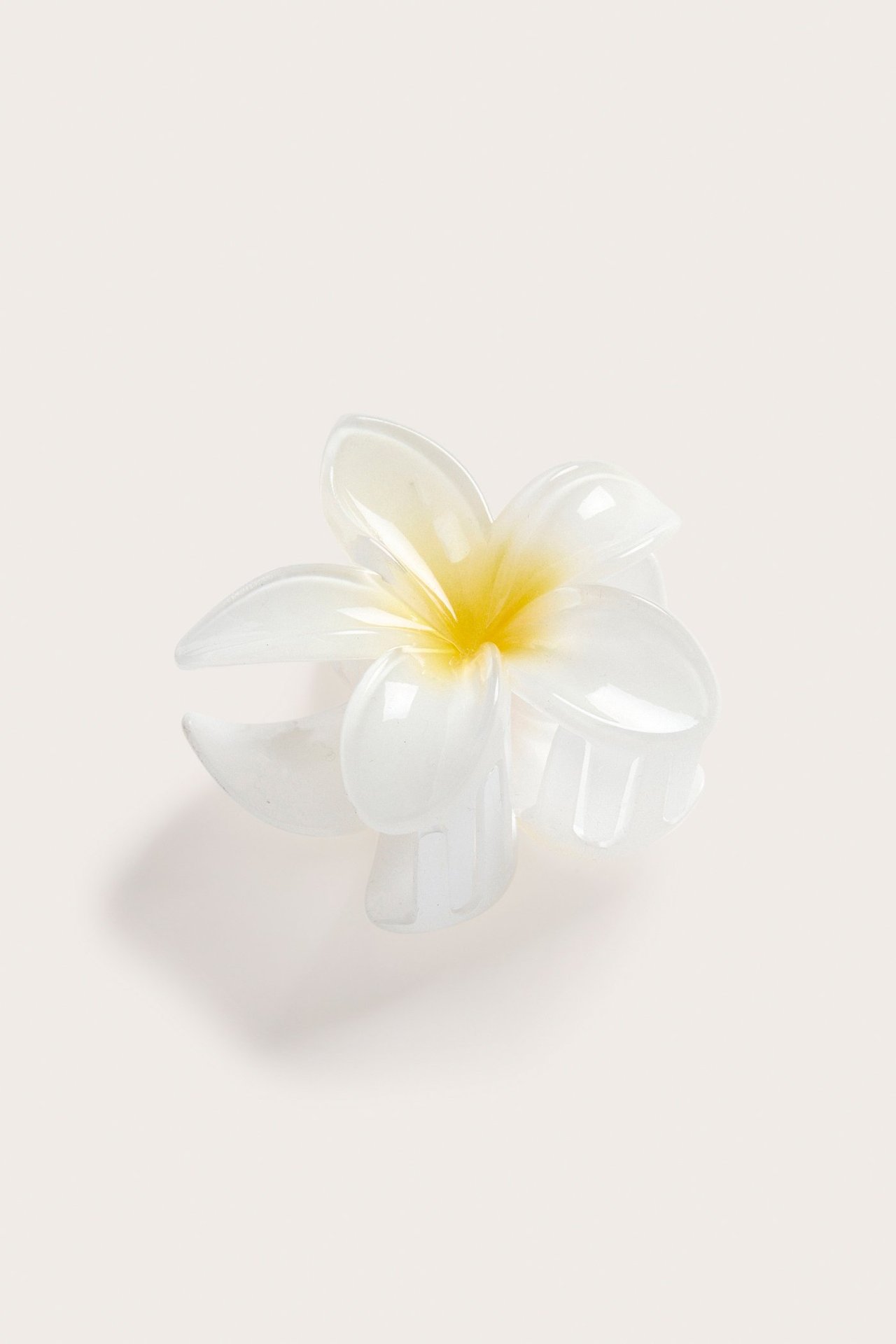 Lähikuva valkoisesta läpikuultavasta kukka-aiheisesta hiusklipsistä keltaisella keskellä.