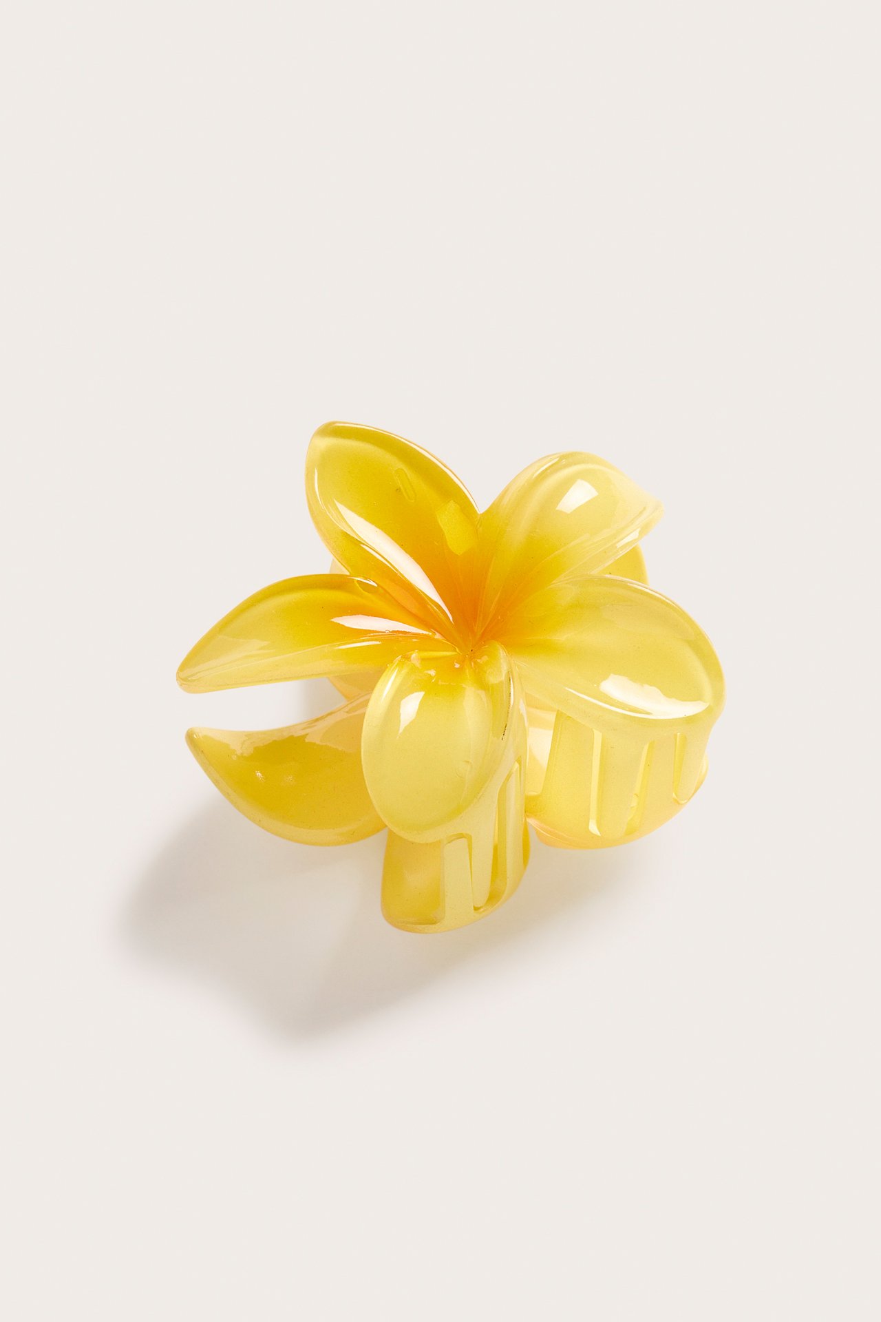 Lähikuva ylhäältä vaaleankeltaisesta kiiltävästä kukkamuotoisesta hiusklipsistä.