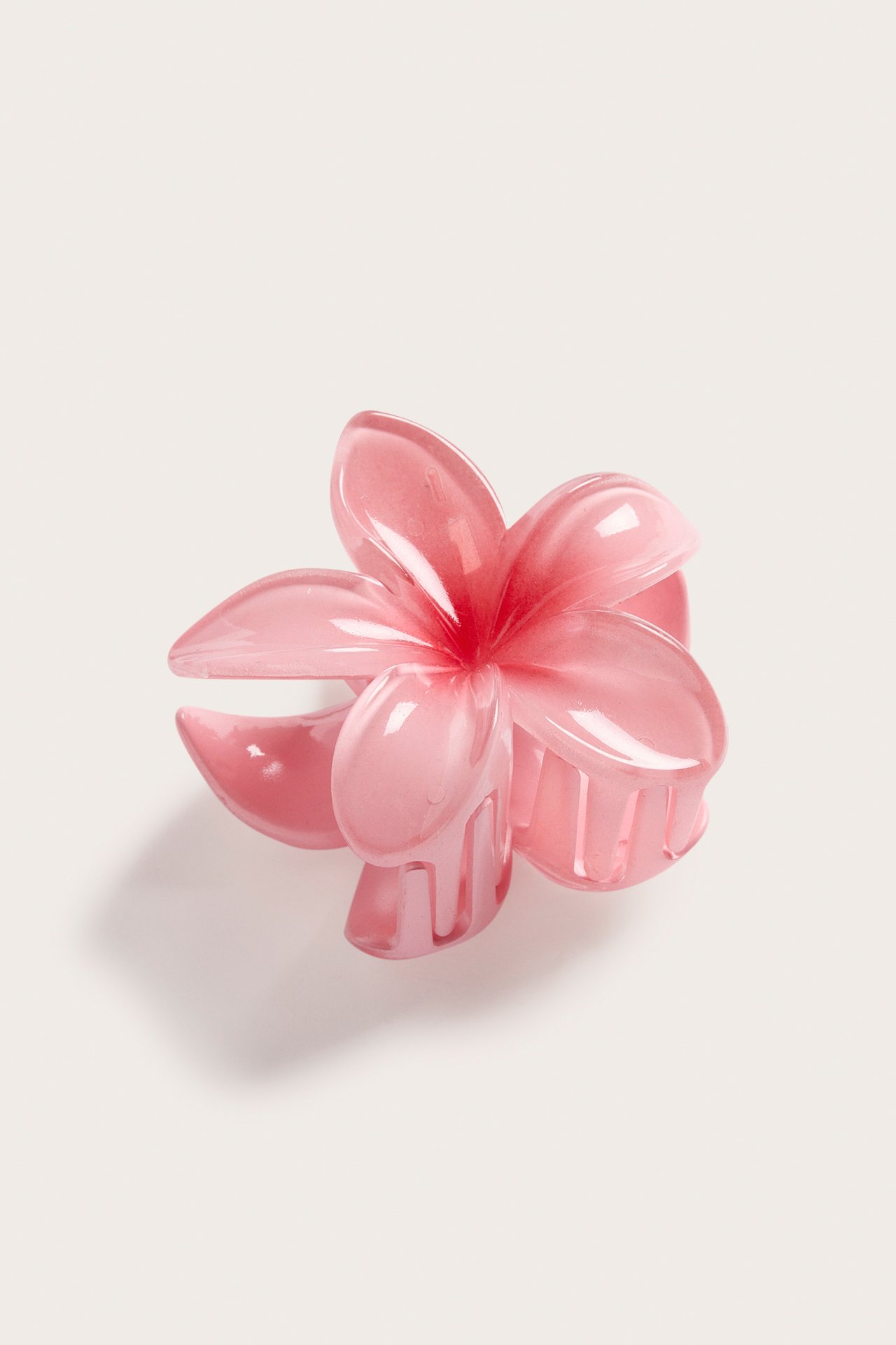 Lähikuva kiiltävästä, läpikuultavasta vaaleanpunaisesta kukka-hiusklipsistä, edestä hieman kulmassa.